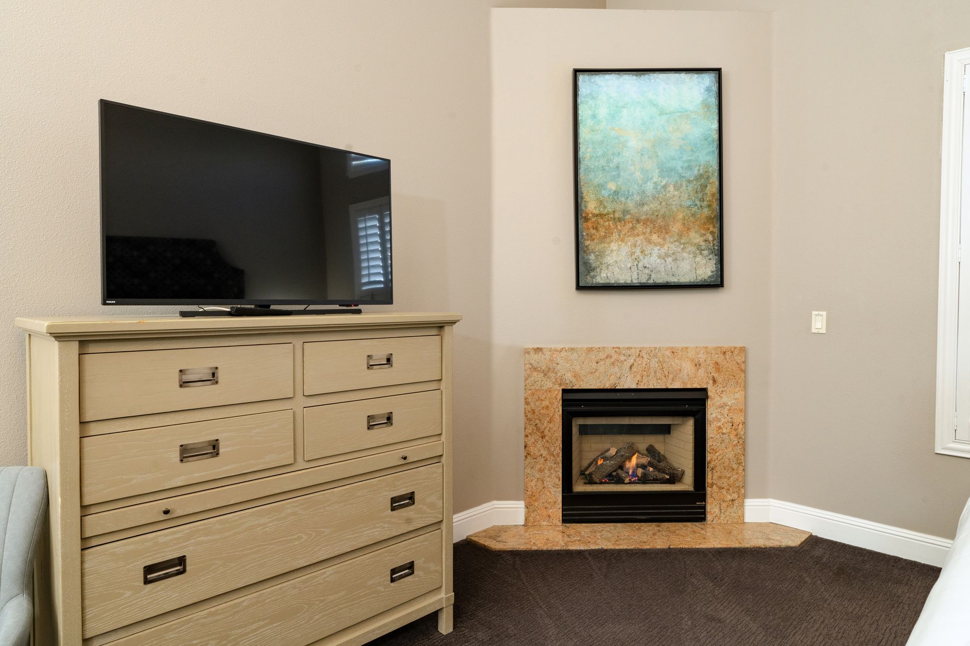A bedroom with a TV on a dresser, fireplace, and abstract art.