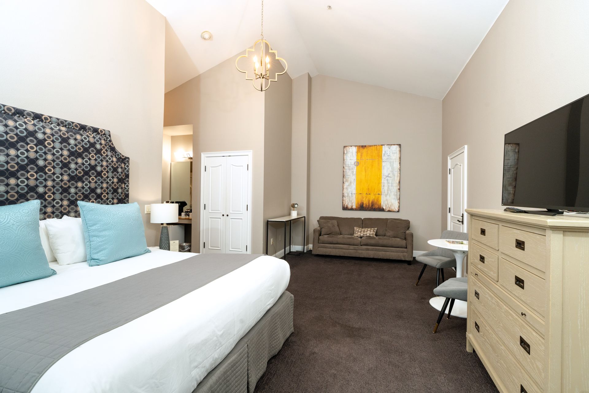 Hotel room with king bed, sofa, dresser, and artwork on the wall.