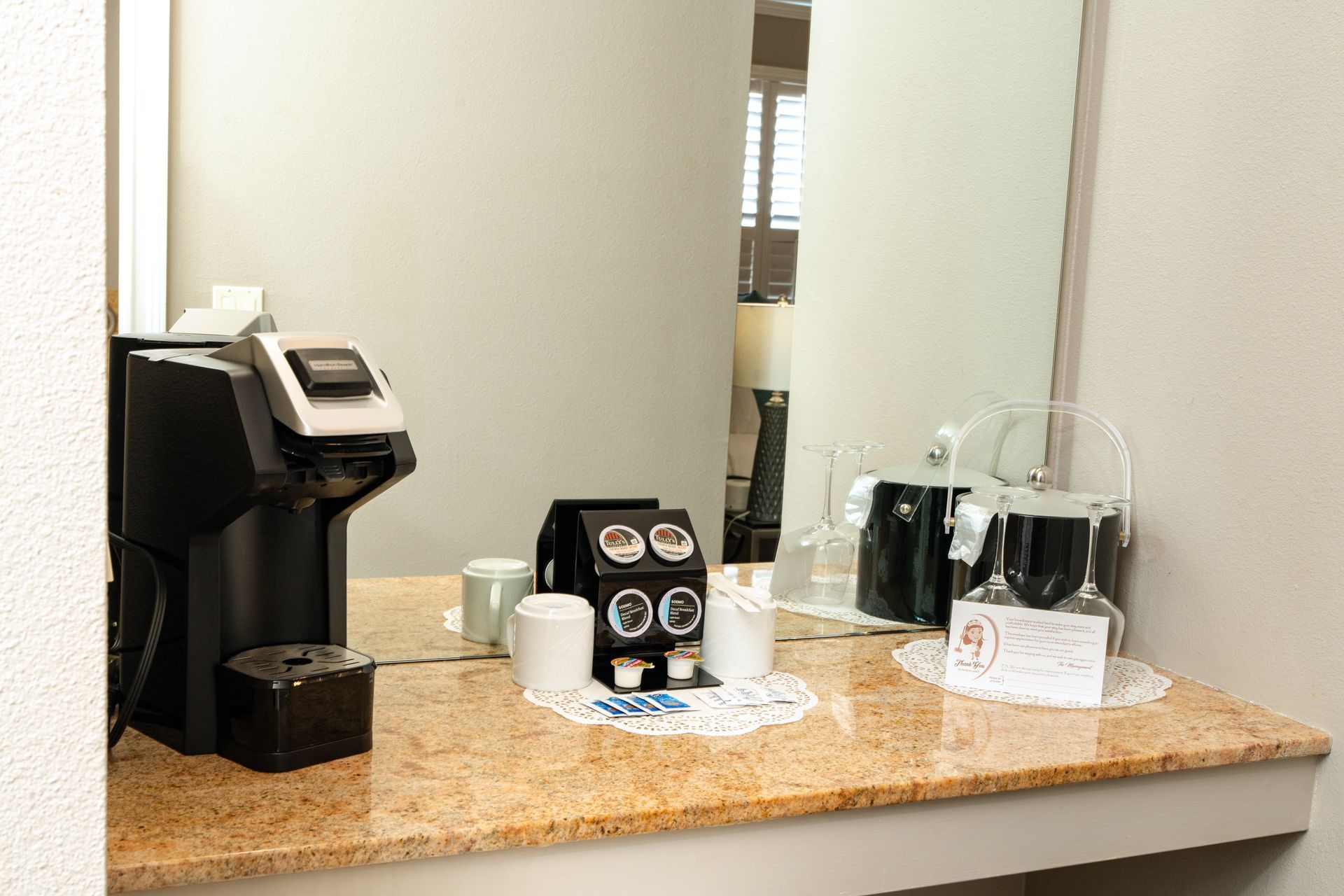 Coffee station on a countertop with Keurig, coffee pods, cups, and a carafe.