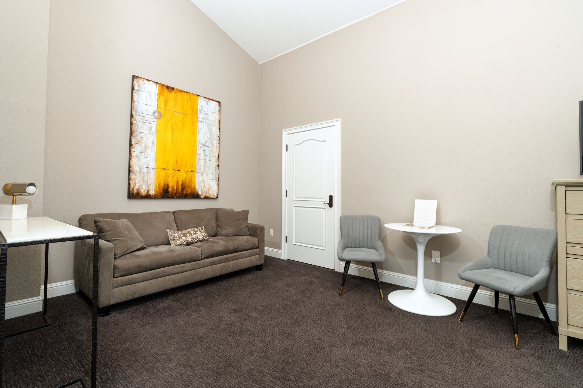 Beige room with sofa, chairs, a table, and abstract art.