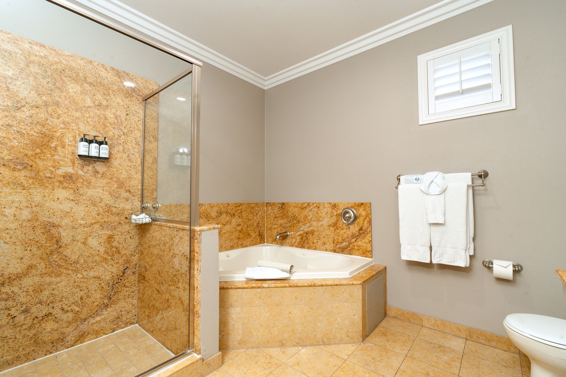 Bathroom with granite shower, bathtub, and toilet. White towels hang on a rack.