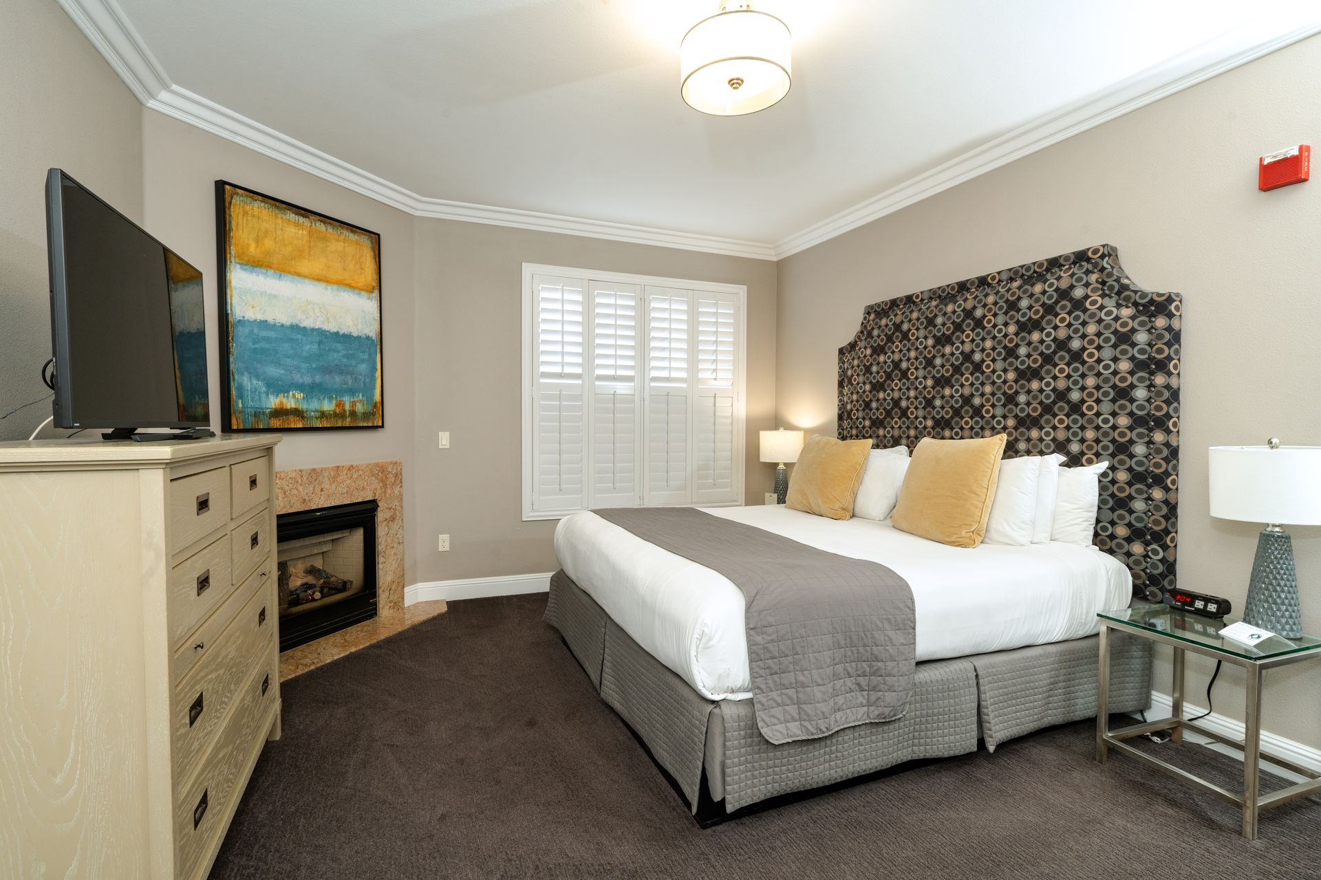 Bedroom with bed, fireplace, dresser, TV, and patterned headboard.