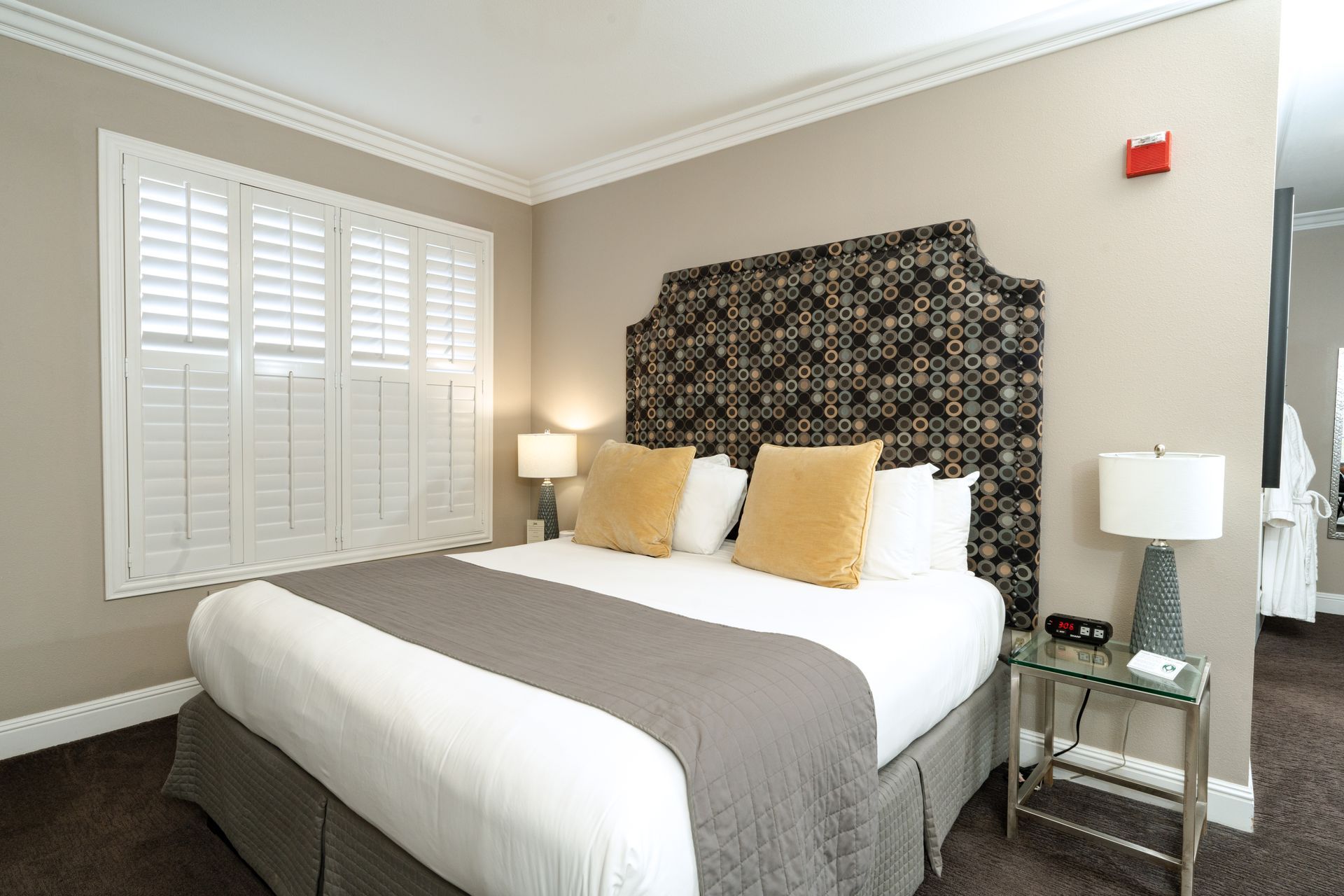 Hotel bedroom with a bed, headboard, window shutters, side tables, and lamps.