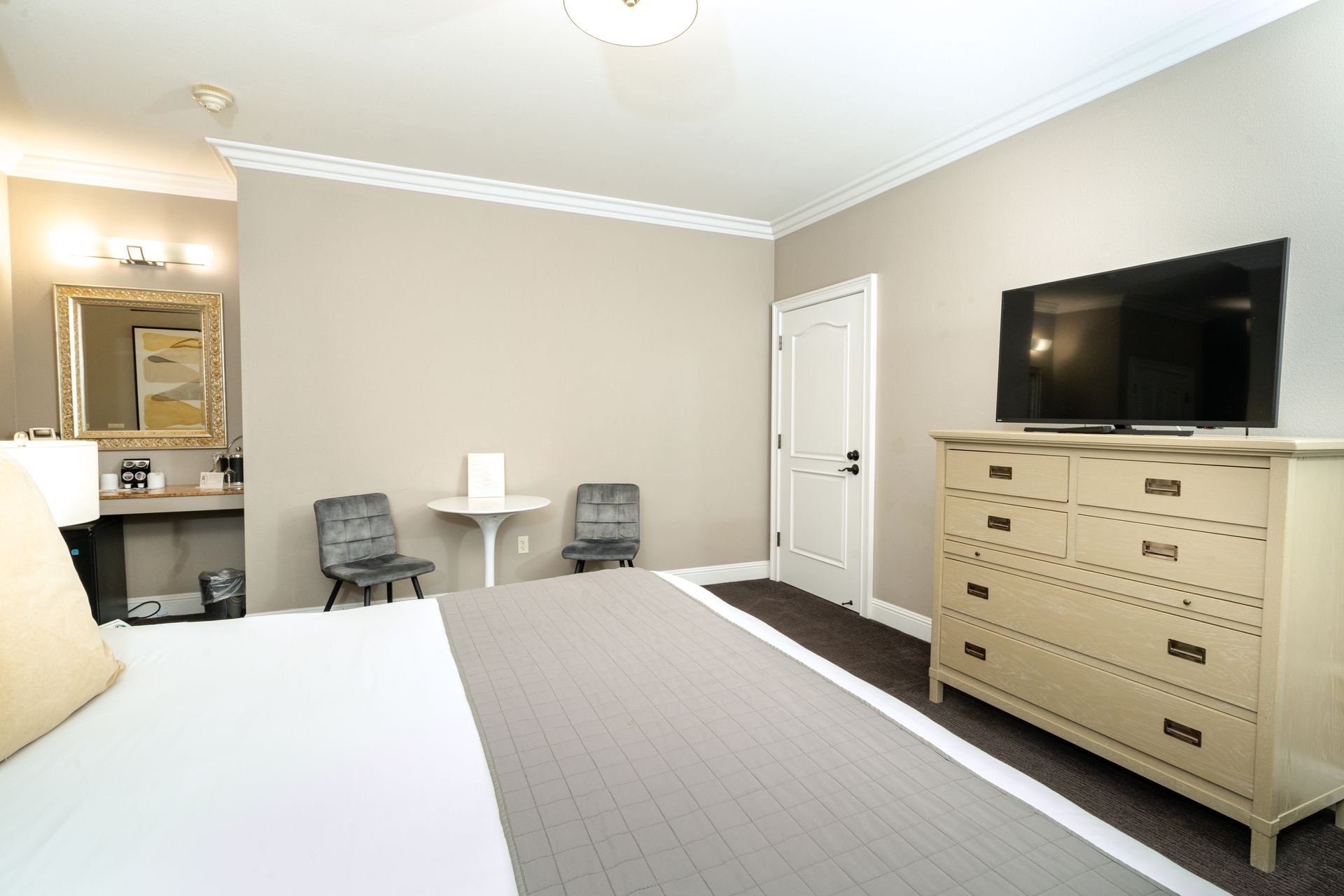 Hotel room with a bed, dresser, table, two chairs, a TV, and a bathroom visible.