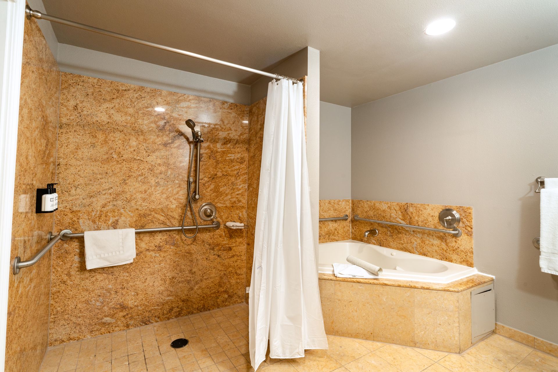 Accessible hotel bathroom with granite shower, tub, grab bars, and shower curtain.