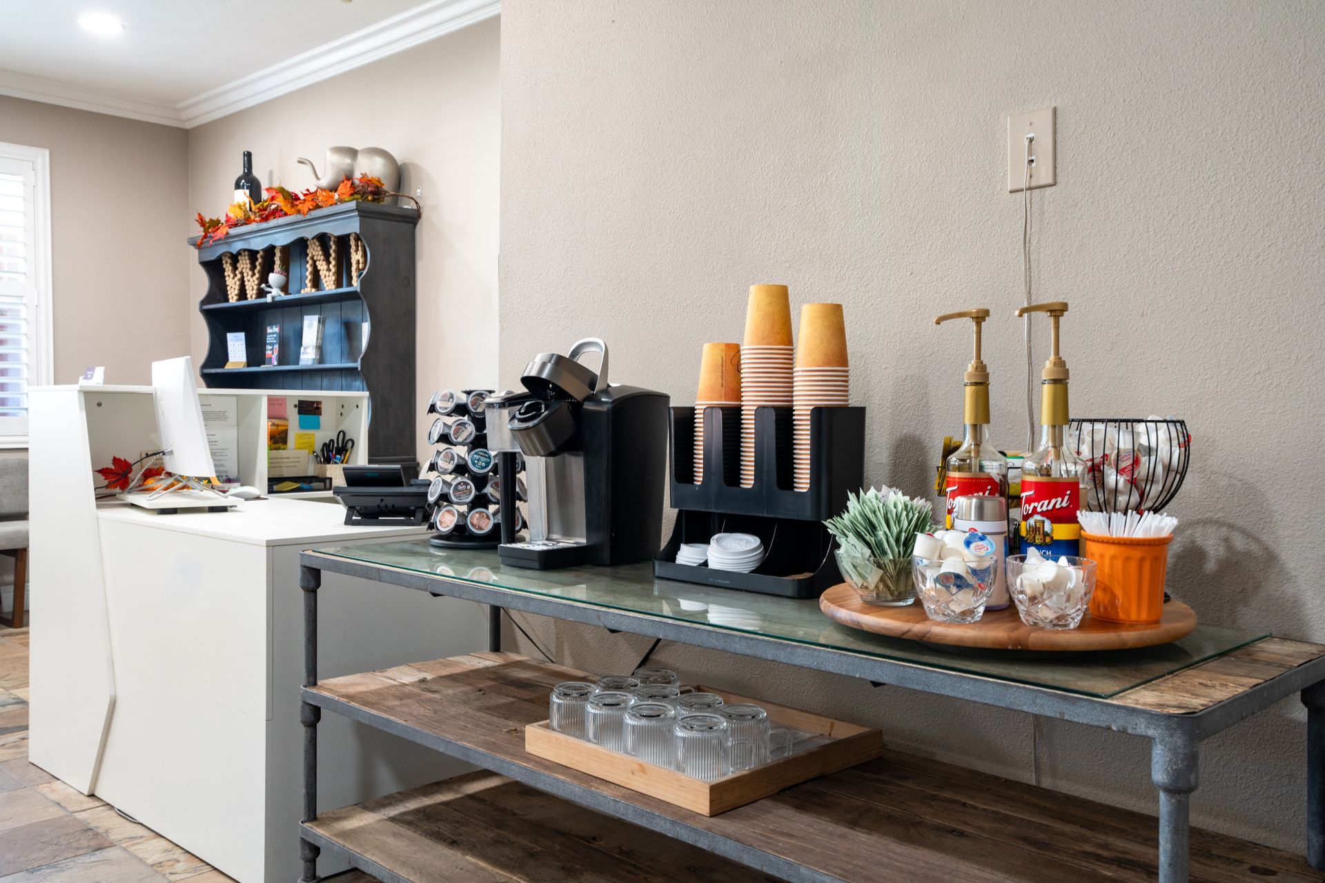 Coffee station with a Keurig, cups, syrups, and snacks on a rustic table.