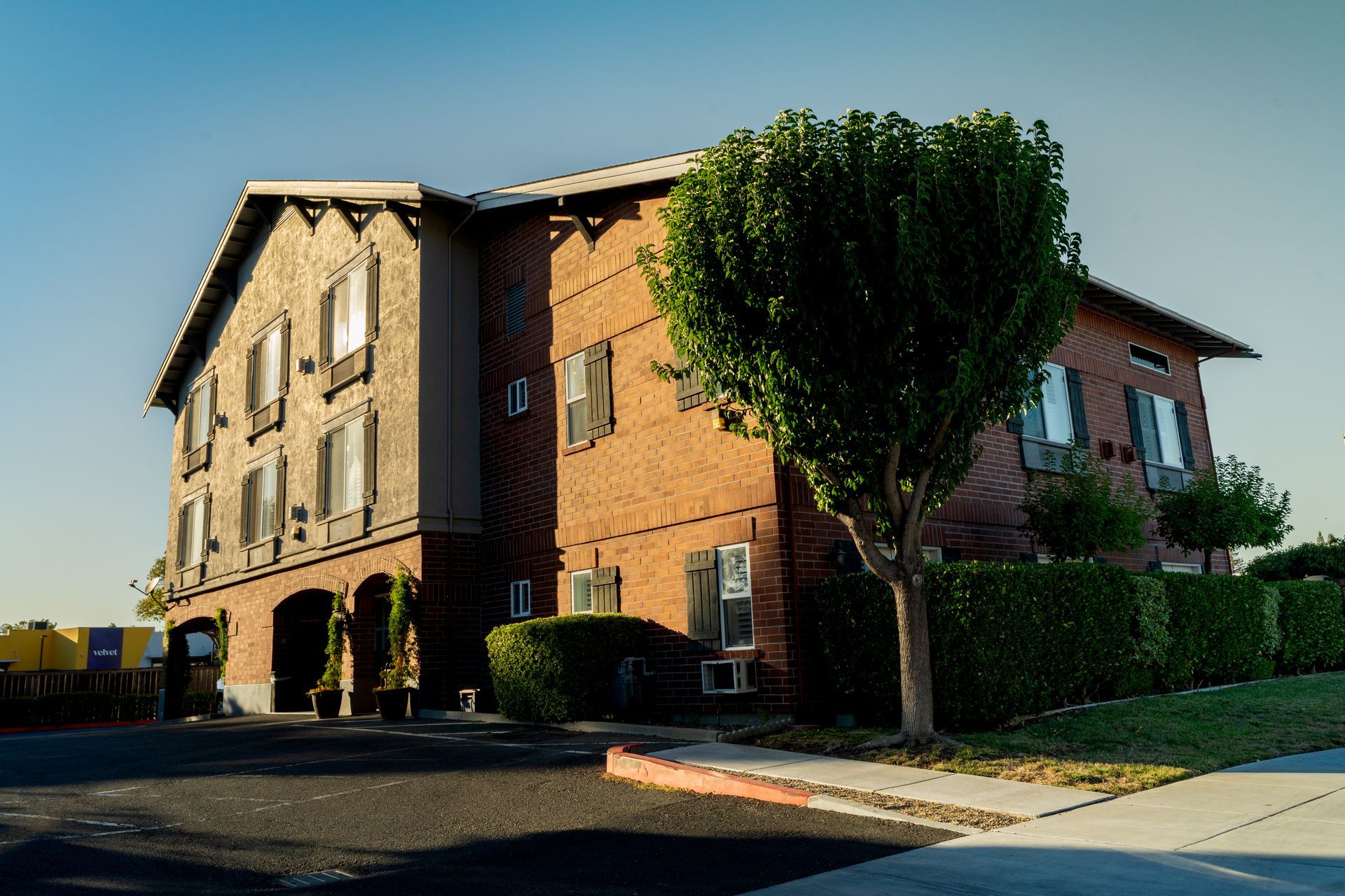 Two-story brick building with arched entryways, brown shutters, and a tree in front.