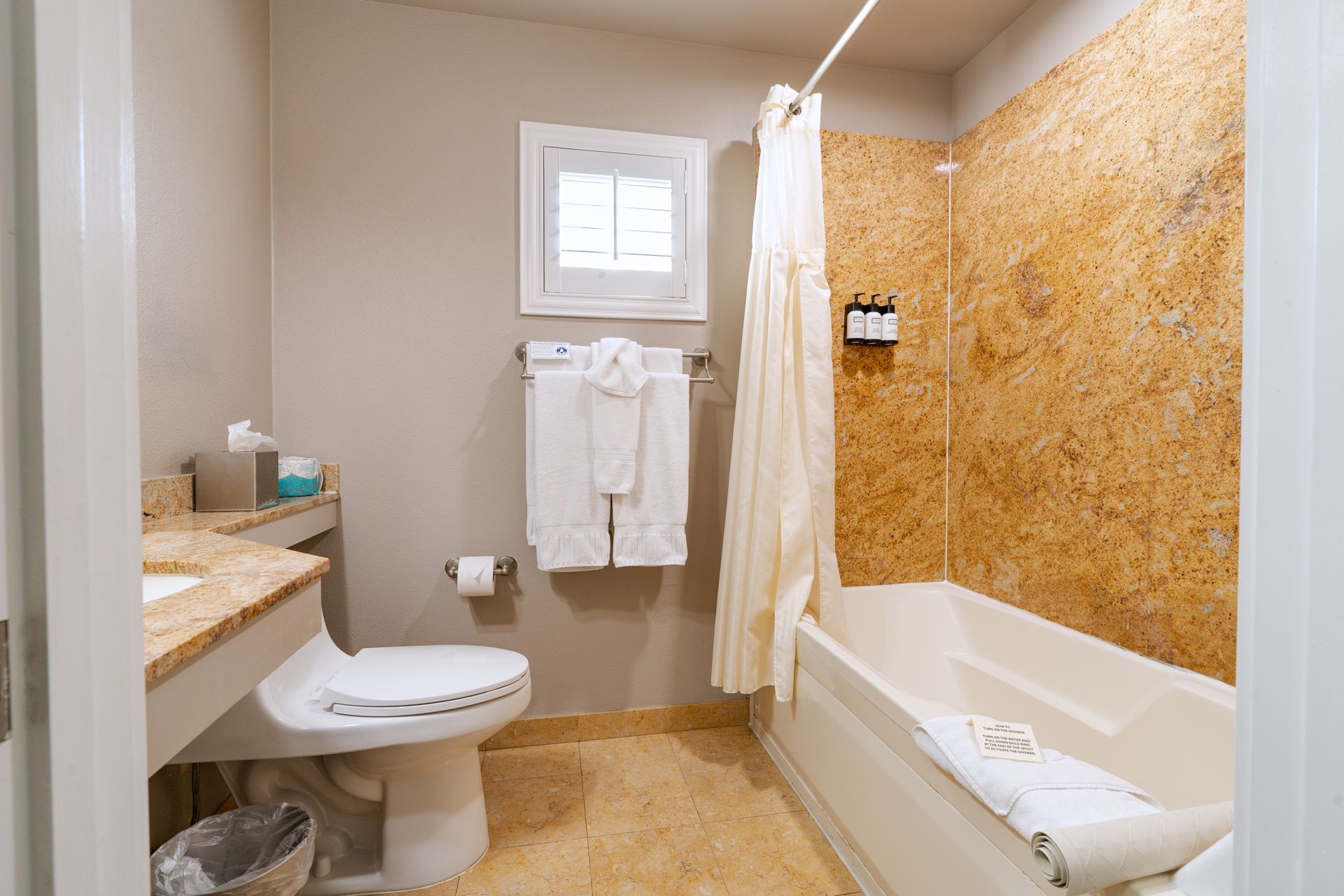 Bathroom with a tub and shower, toilet, sink, and towels; beige walls and floor.