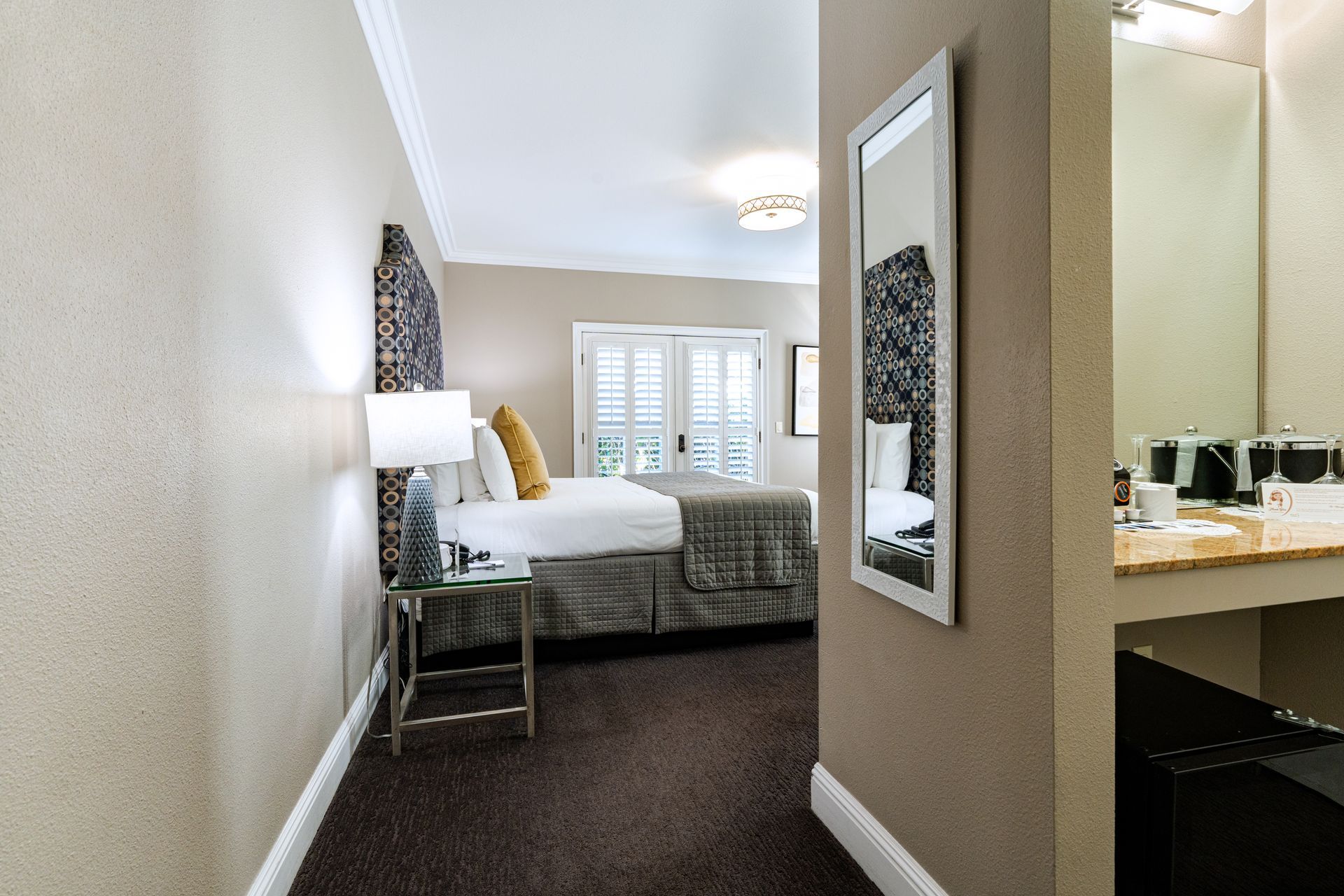 Hotel room hallway with bed, mirror, and bathroom vanity visible.