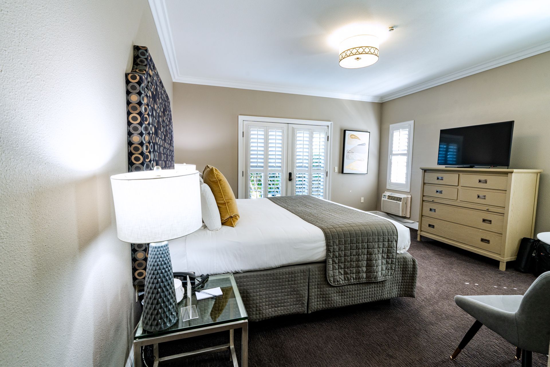 Bedroom with a bed, dresser, TV, and French doors leading outside; neutral colors.