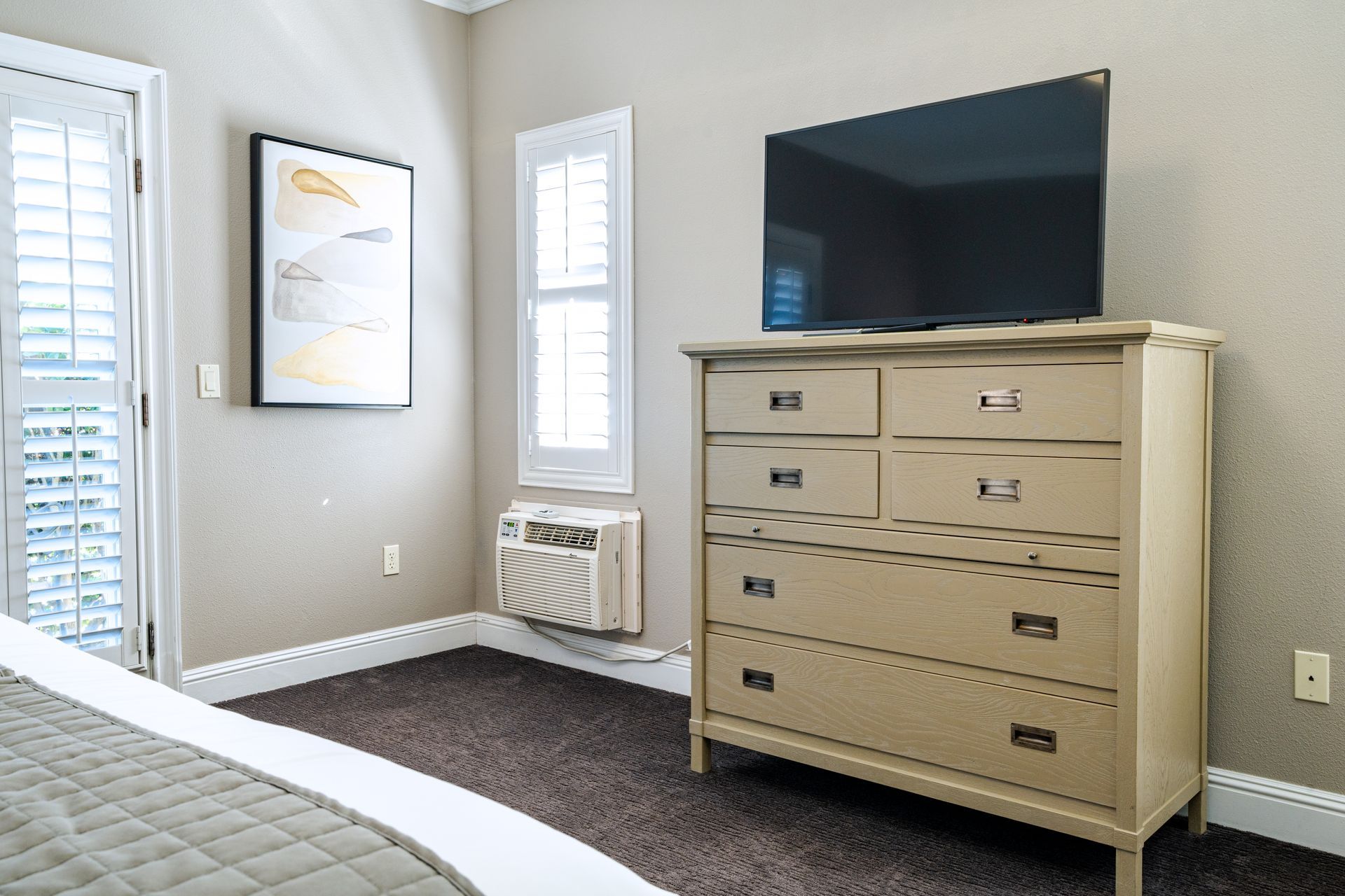 Bedroom with dresser, TV, window with shutters, and an air conditioner.