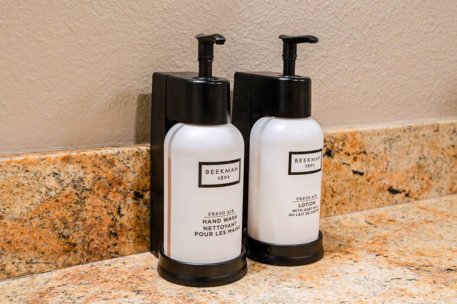 Two white soap dispensers with black pumps in a black holder on a marble countertop.