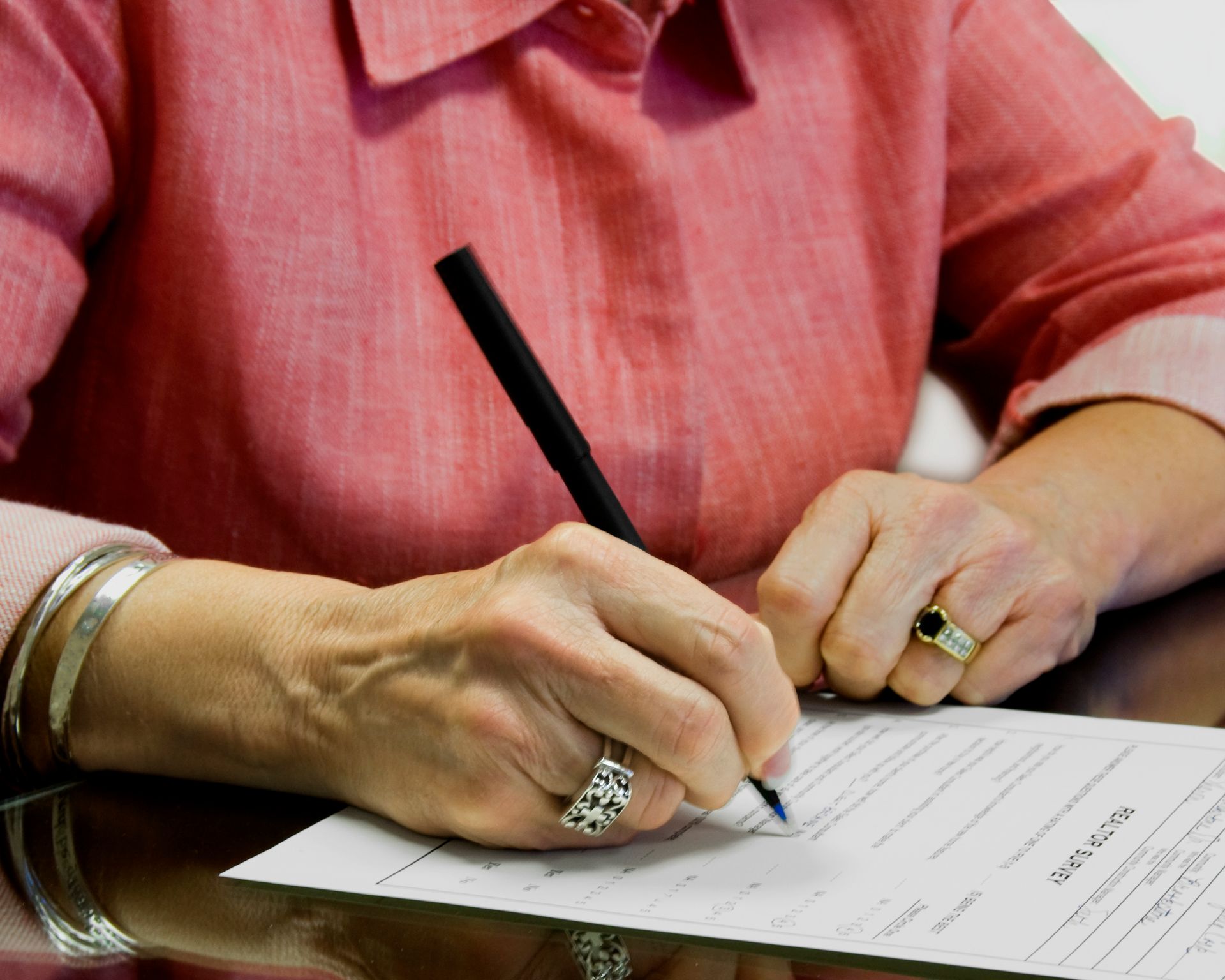 A woman in a pink shirt is writing on a piece of paper