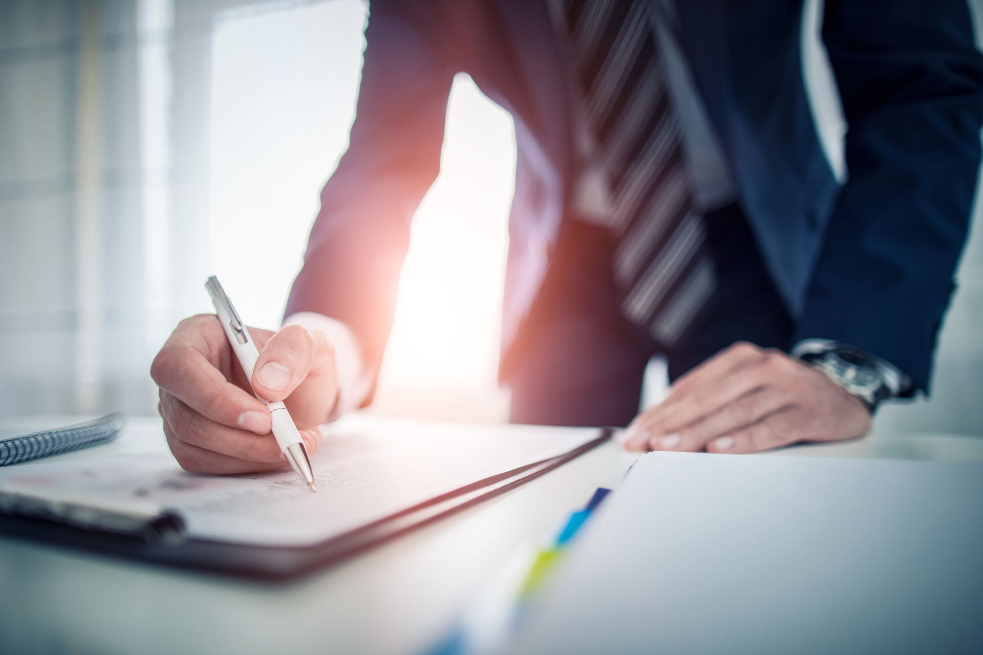 A man in a suit and tie is signing a document on a clipboard.