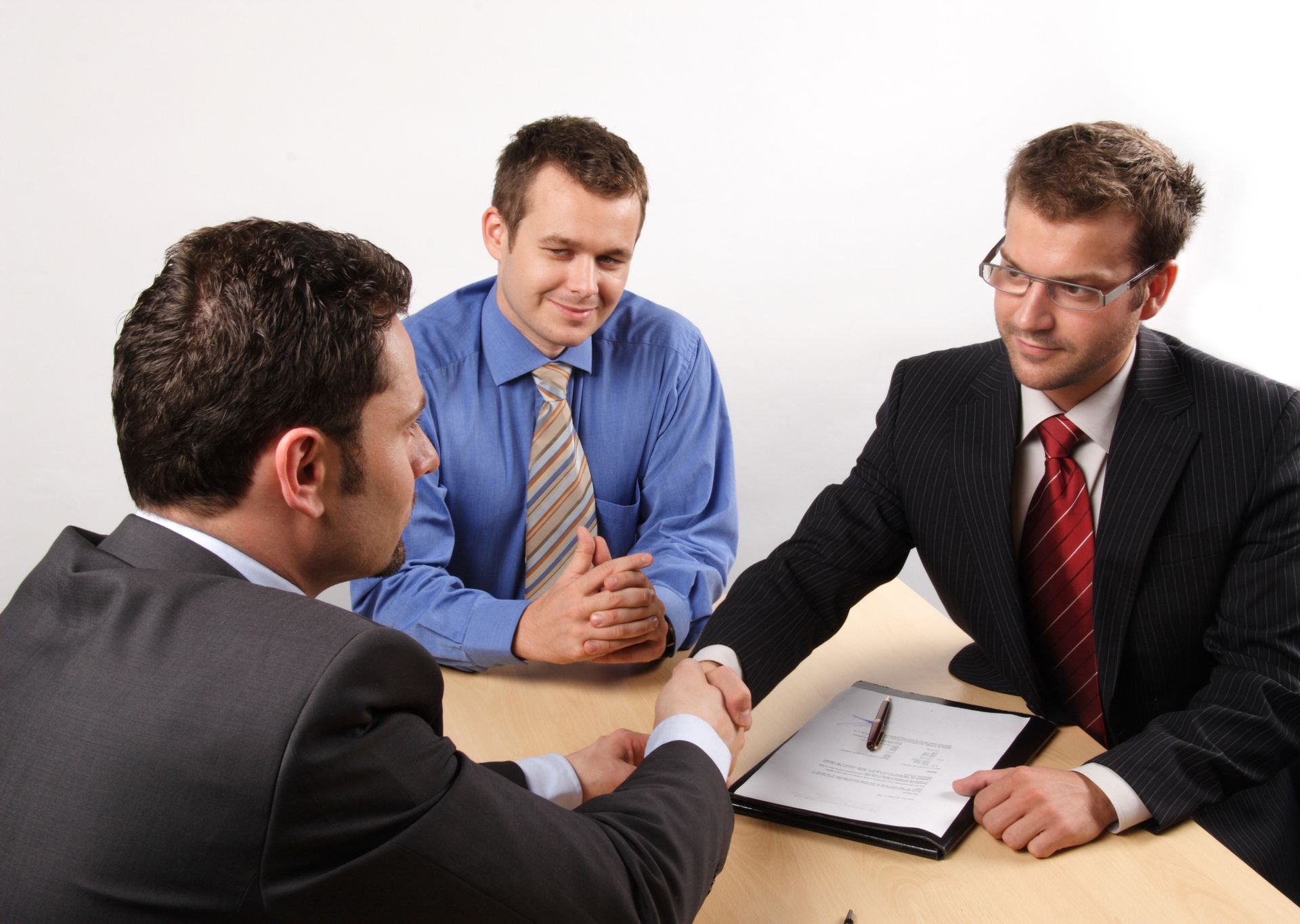 Three men are sitting at a table shaking hands