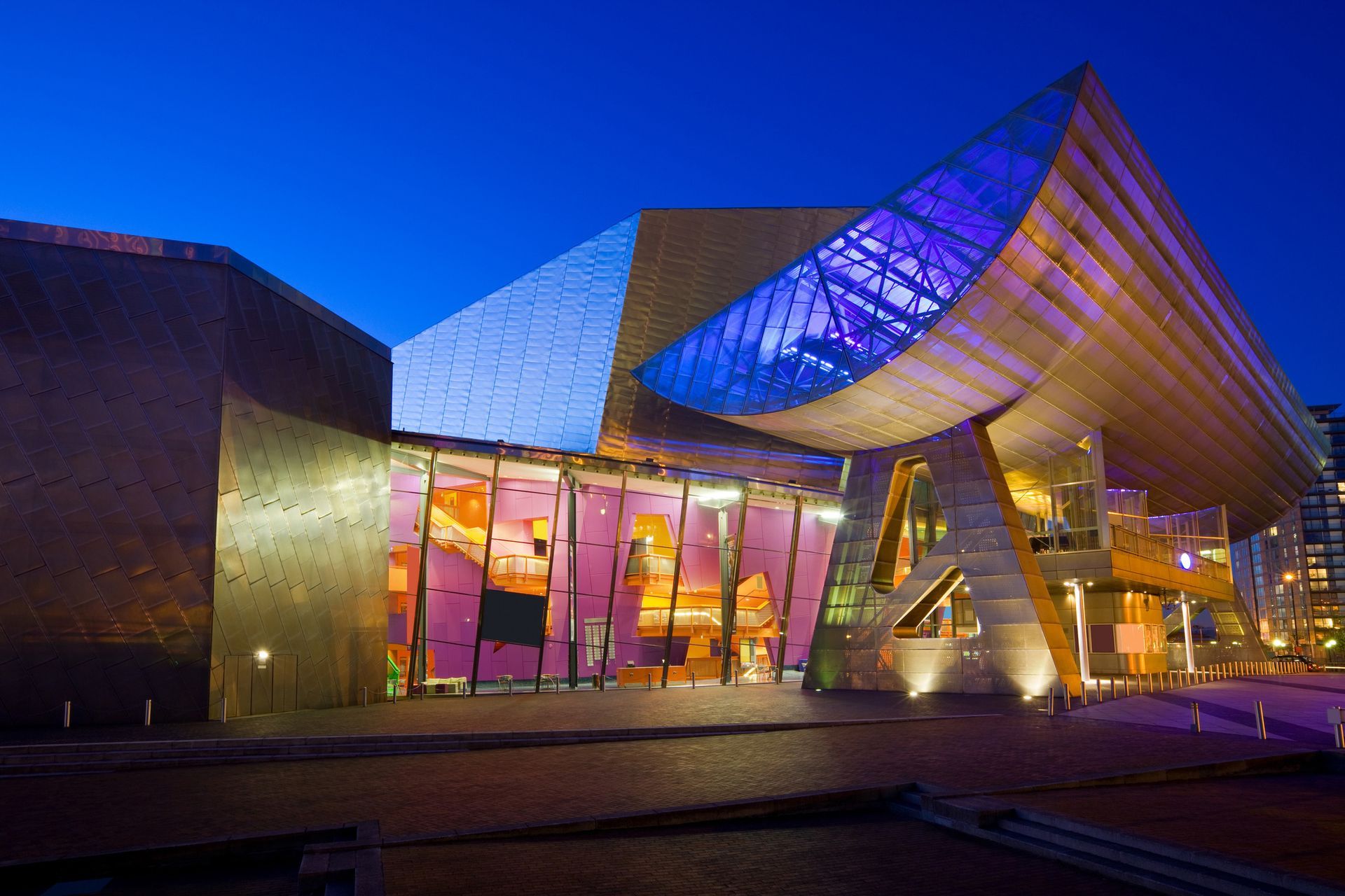 A large building with a blue sky in the background is lit up at night.