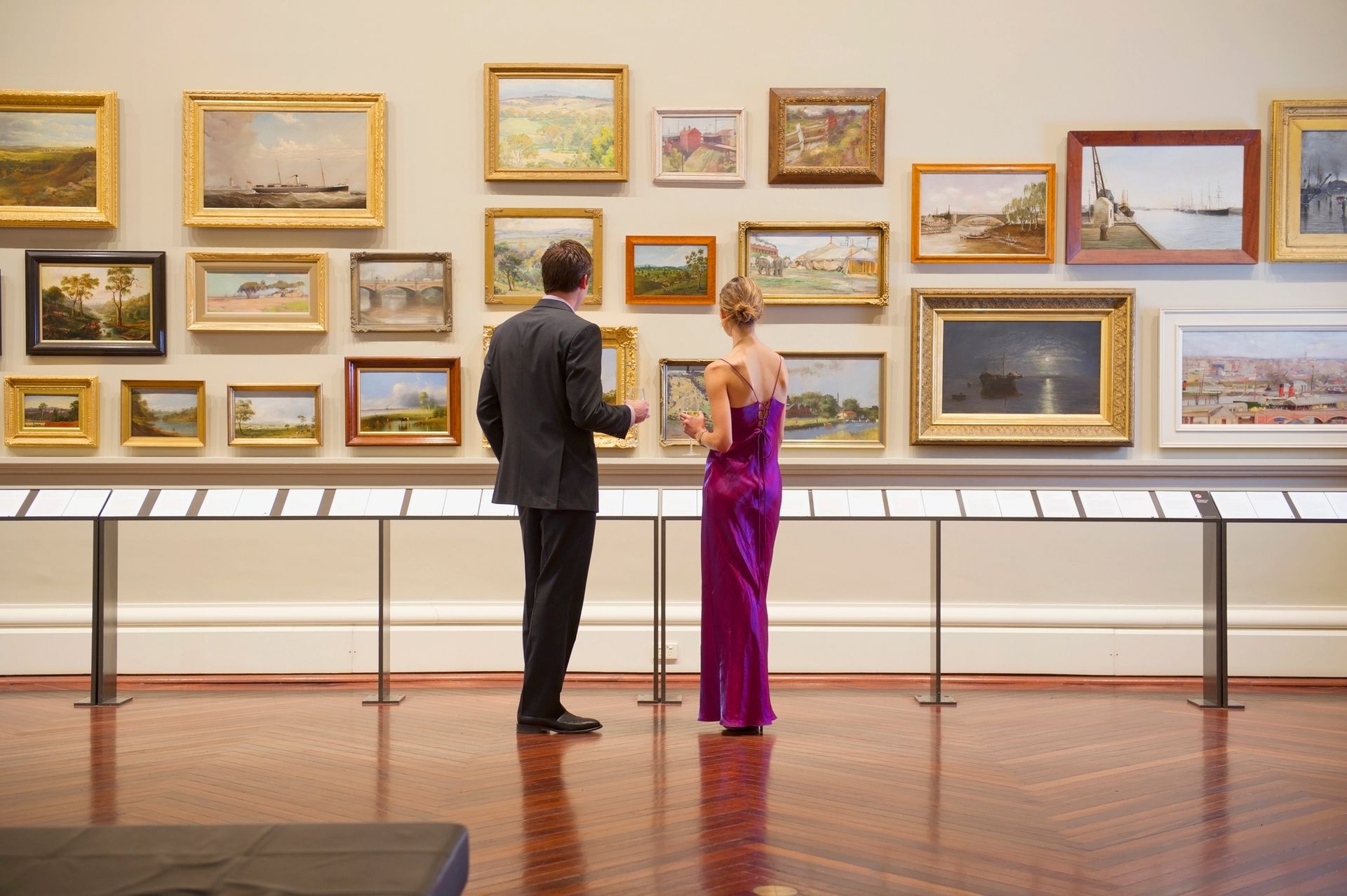 A man and a woman are looking at paintings in a museum.