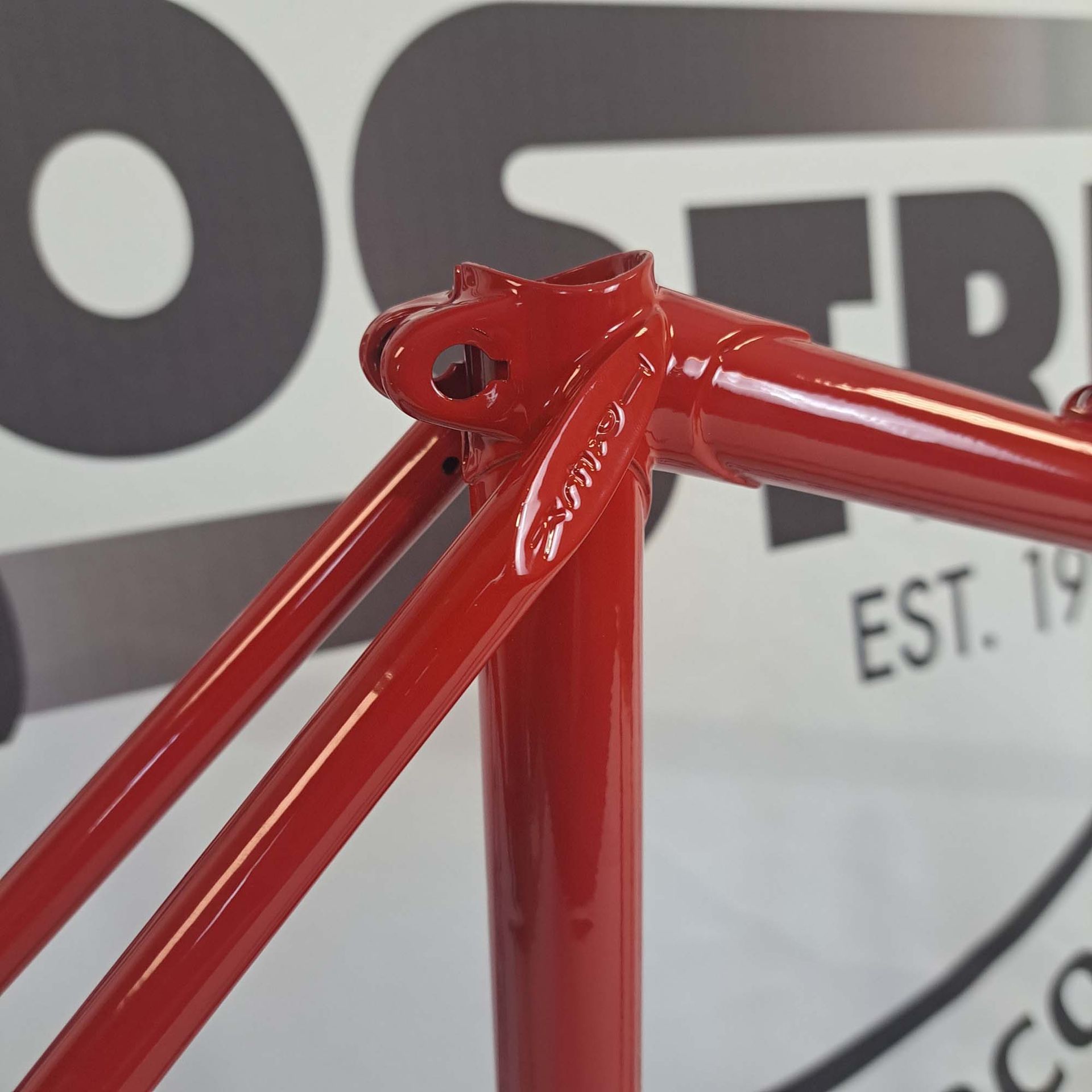 A red bicycle frame is sitting in front of a sign that says est 19