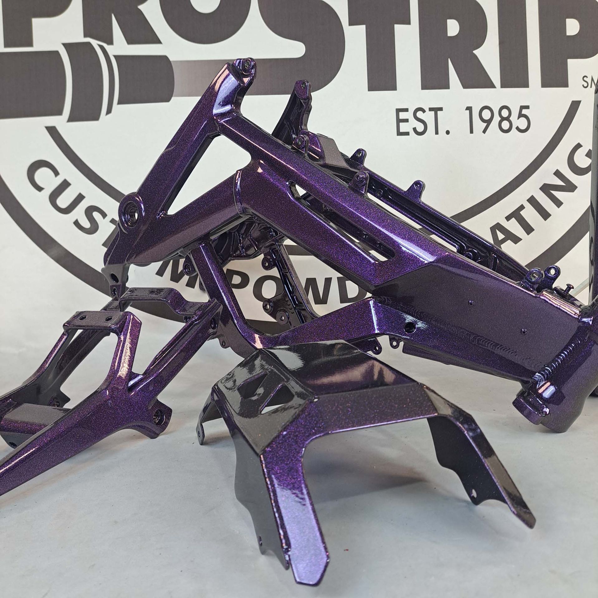 A purple motorcycle frame is sitting in front of a pro strip logo