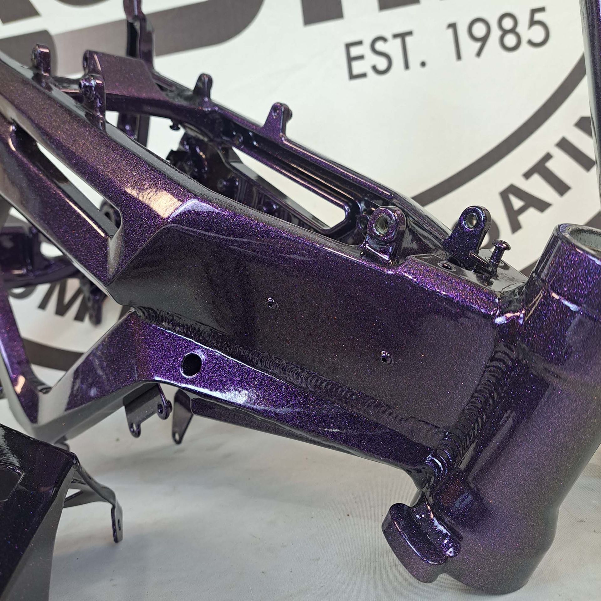 A purple motorcycle frame is sitting in front of a 1985 sign