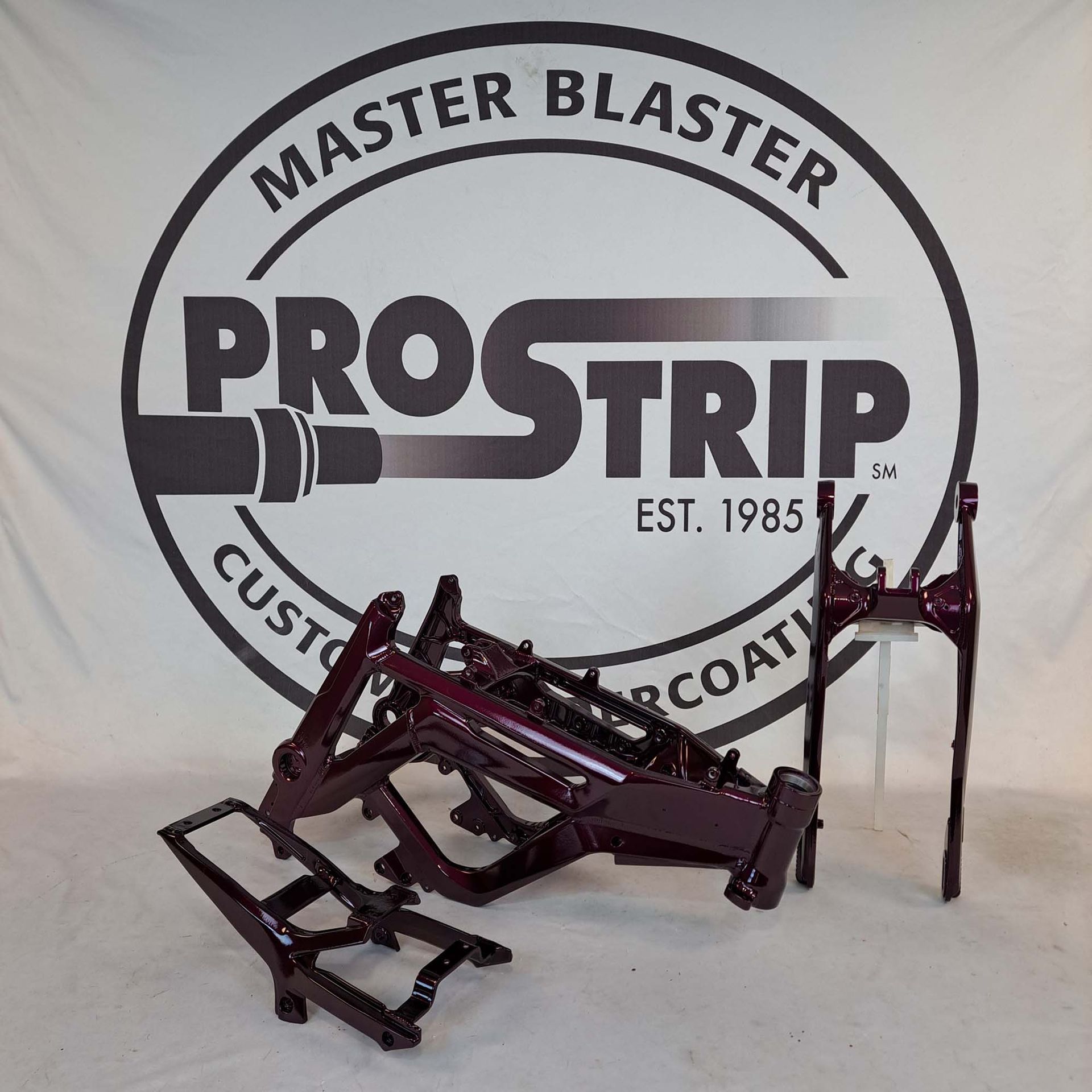 A motorcycle frame is sitting in front of a master blaster prostrip logo