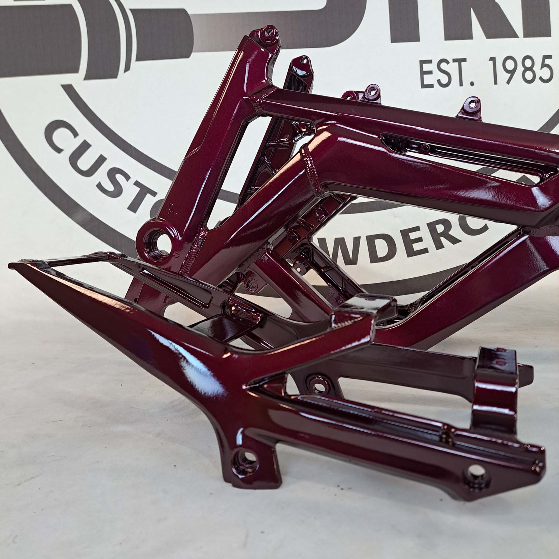 A purple motorcycle frame is sitting in front of a sign that says custom