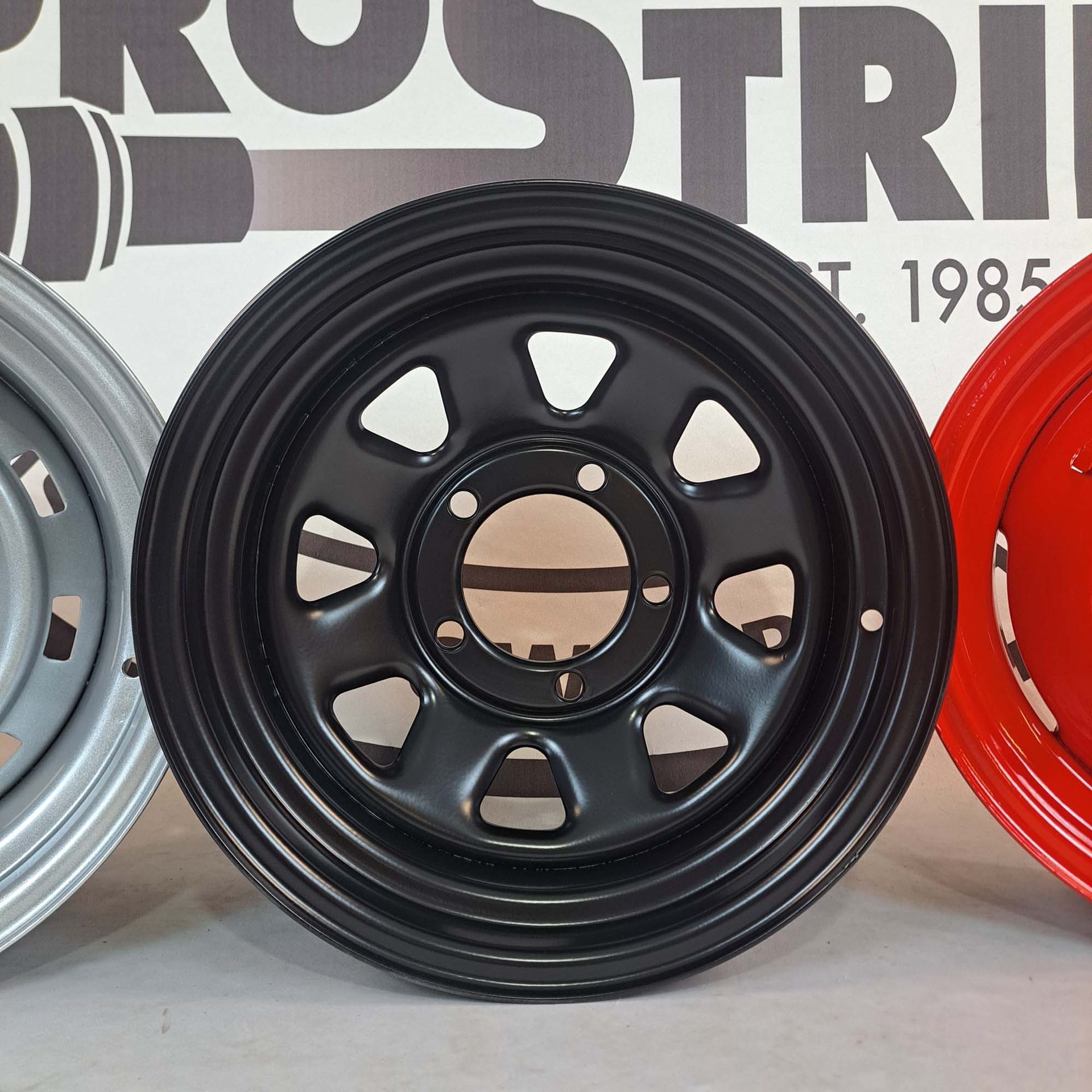 Three different colored wheels are lined up in front of a 1985 sign