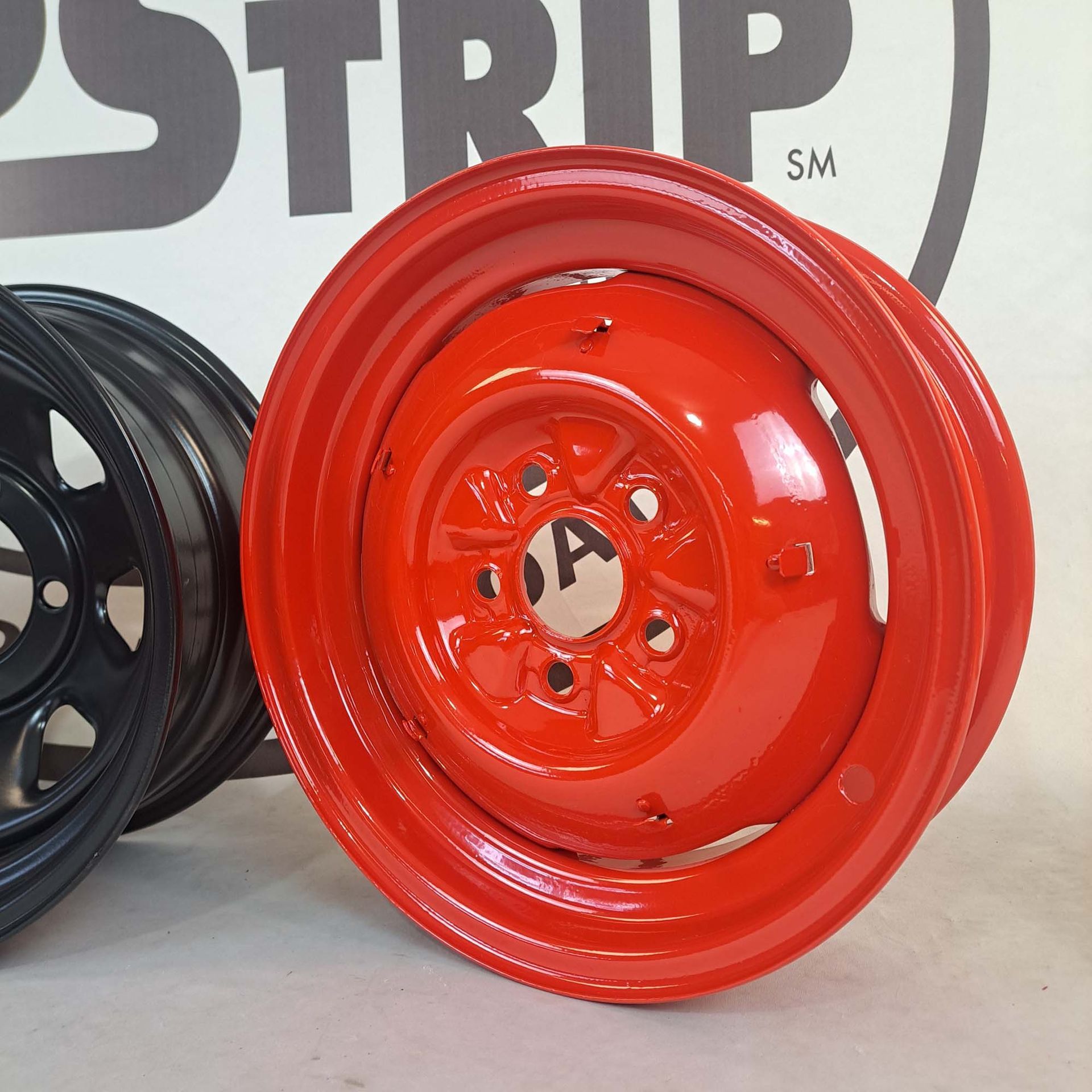 A red rim sits next to a black rim in front of a sign that says strip sm