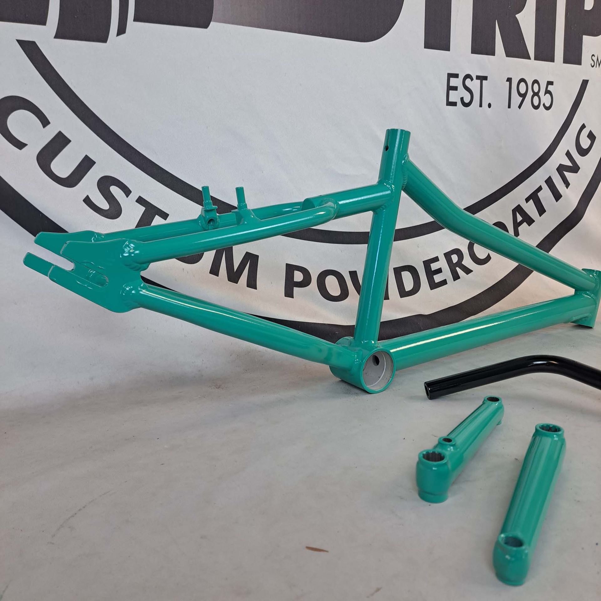 A green bicycle frame is sitting in front of a sign that says custom powdercoating