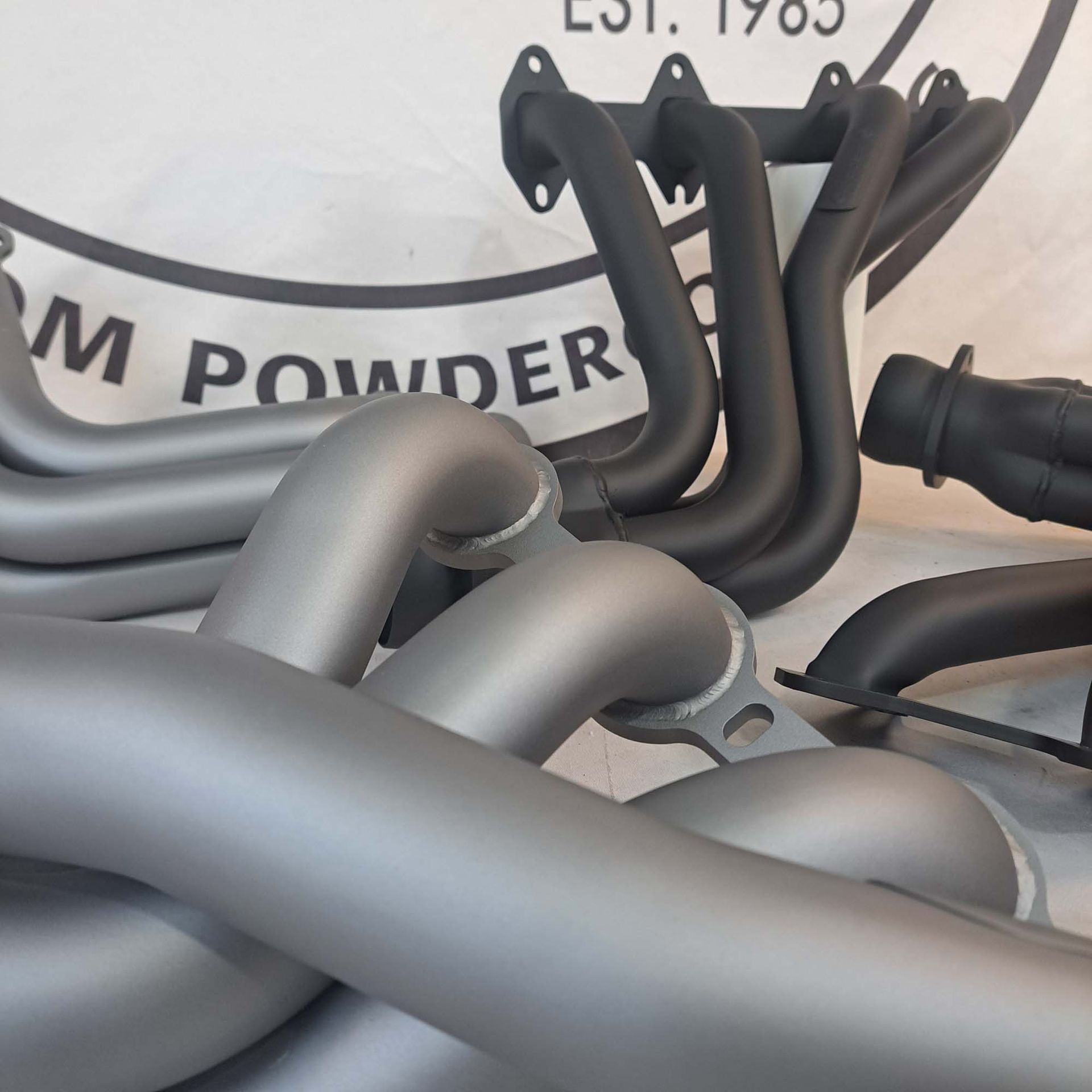 A bunch of exhaust pipes are sitting in front of a sign that says ' m powder '