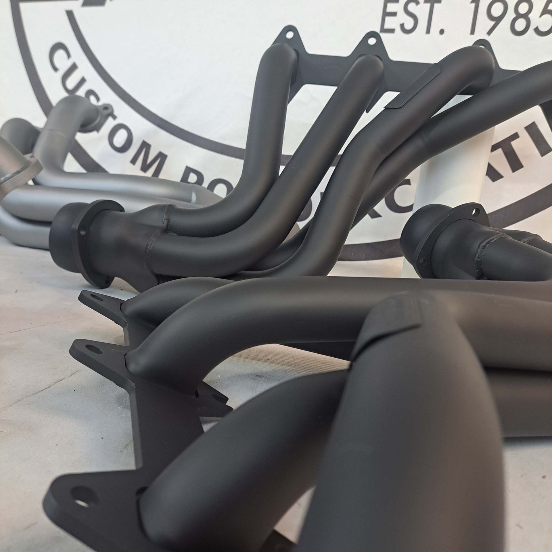 Exhaust pipes are sitting in front of a sign that says custom