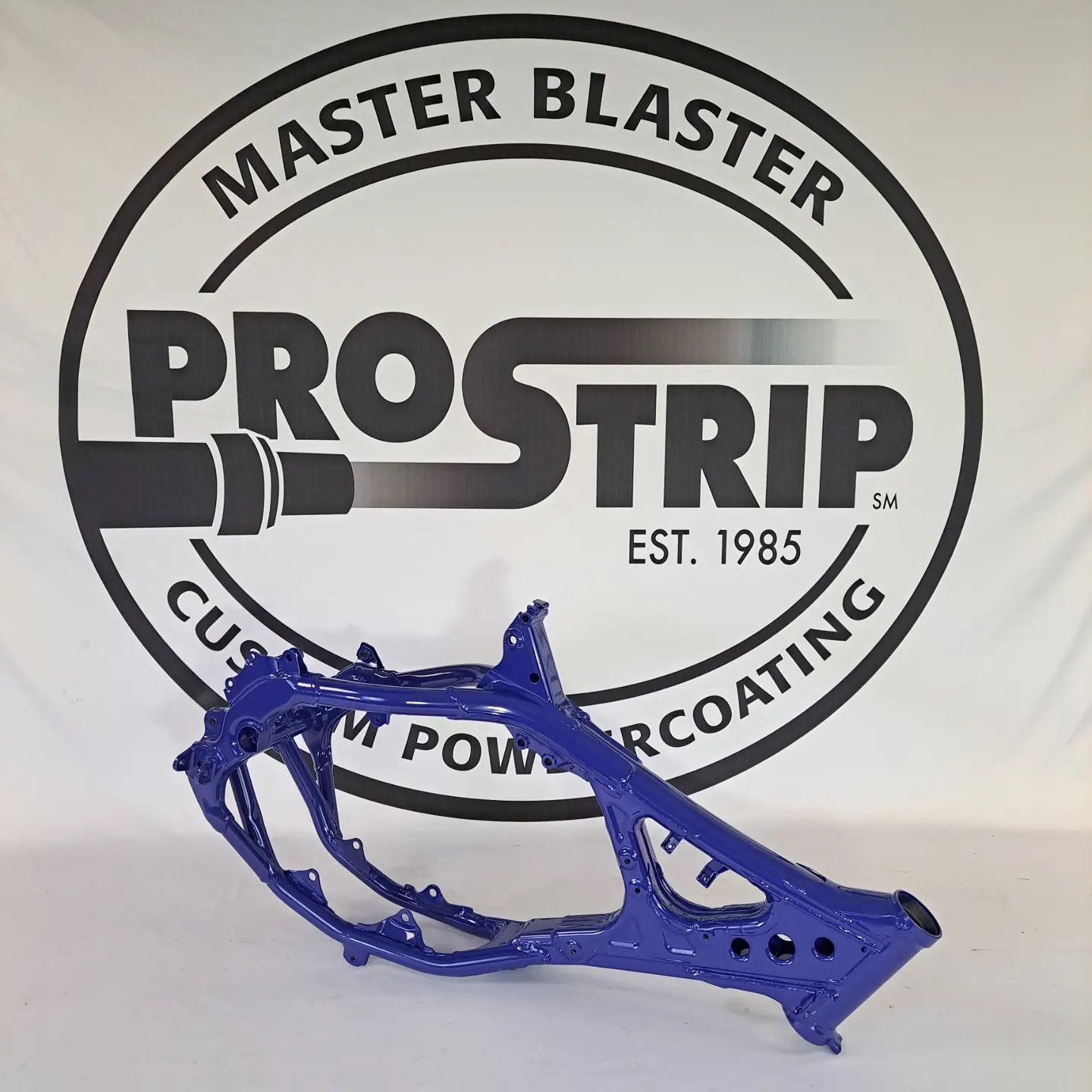 A blue motorcycle frame is sitting in front of a master blaster prostrip logo