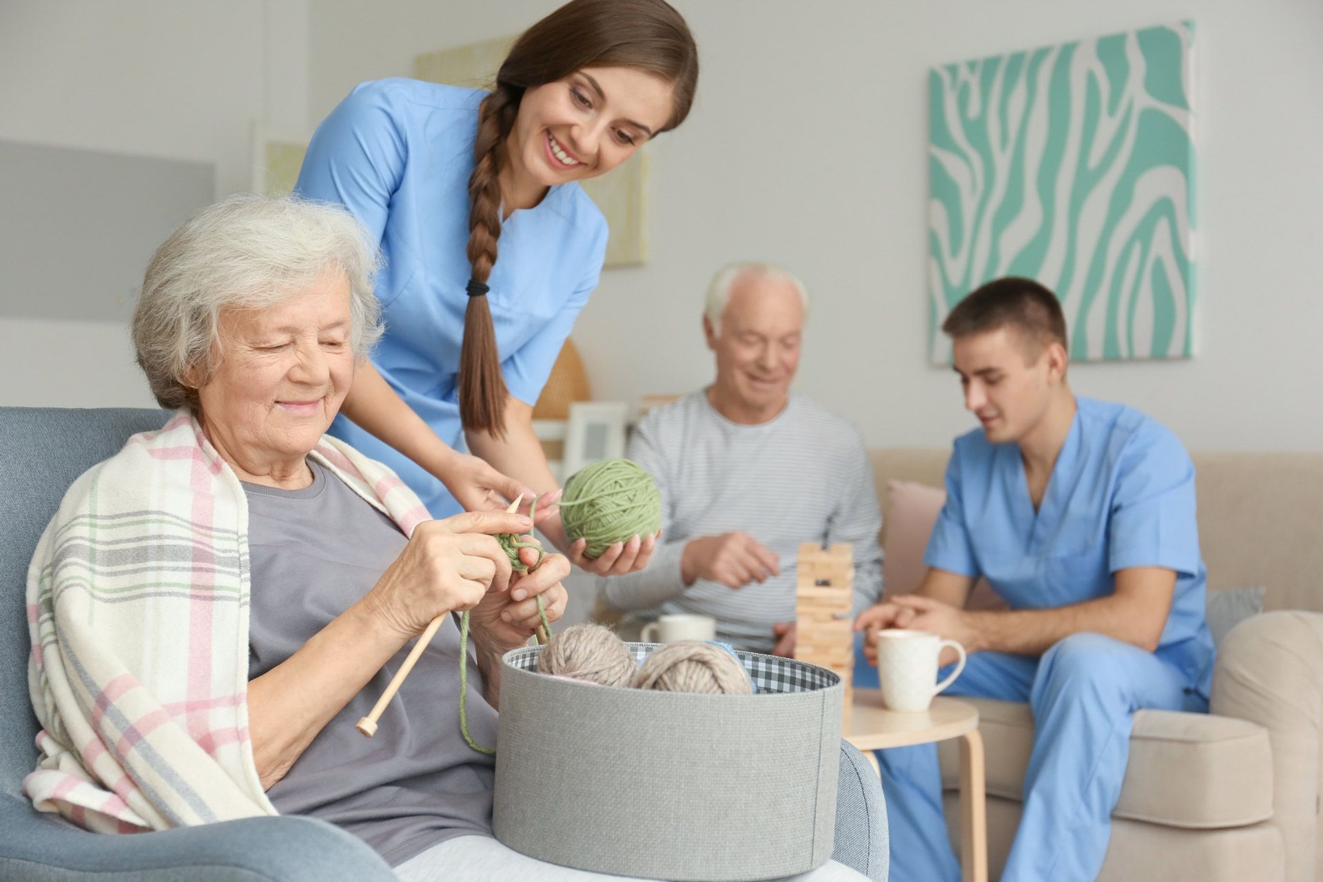 Senior woman knitting with assistance of her caregiver at home.