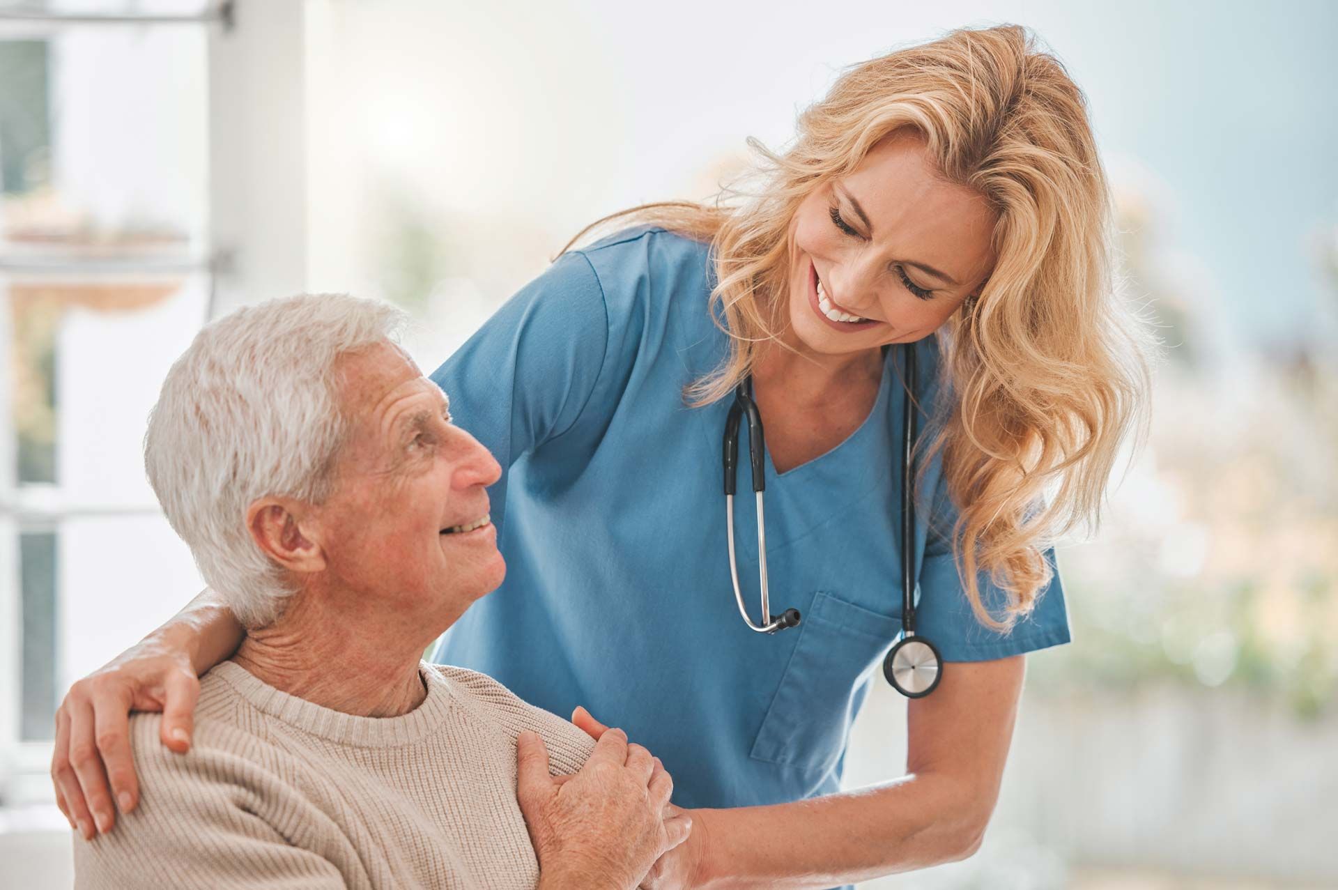 A nurse and a senior man are smiling at each other at his assisted living home.