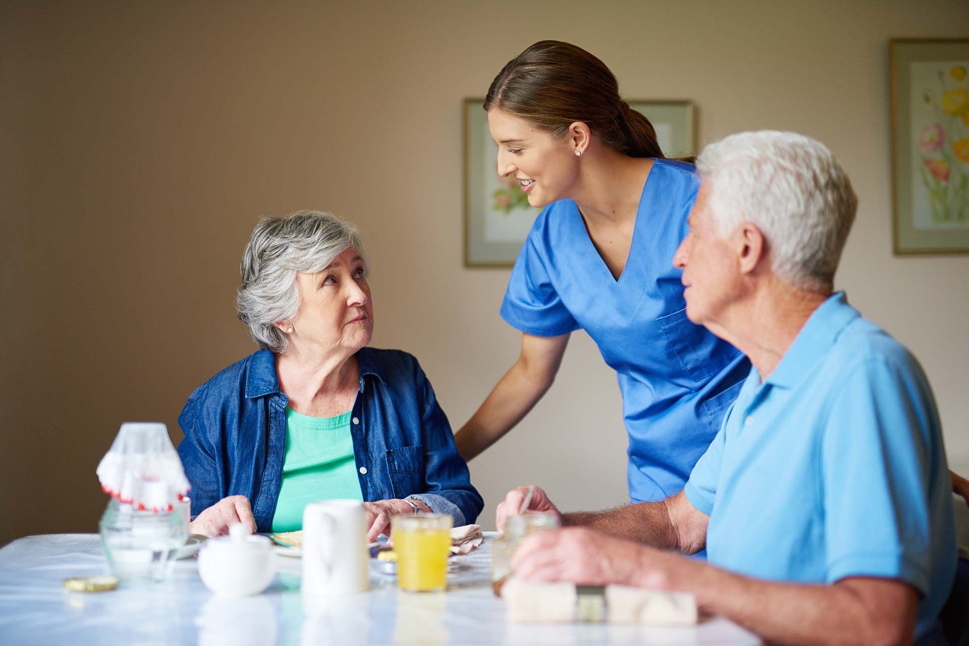 A nurse and a senior couple in a dining room of an assisted living home.