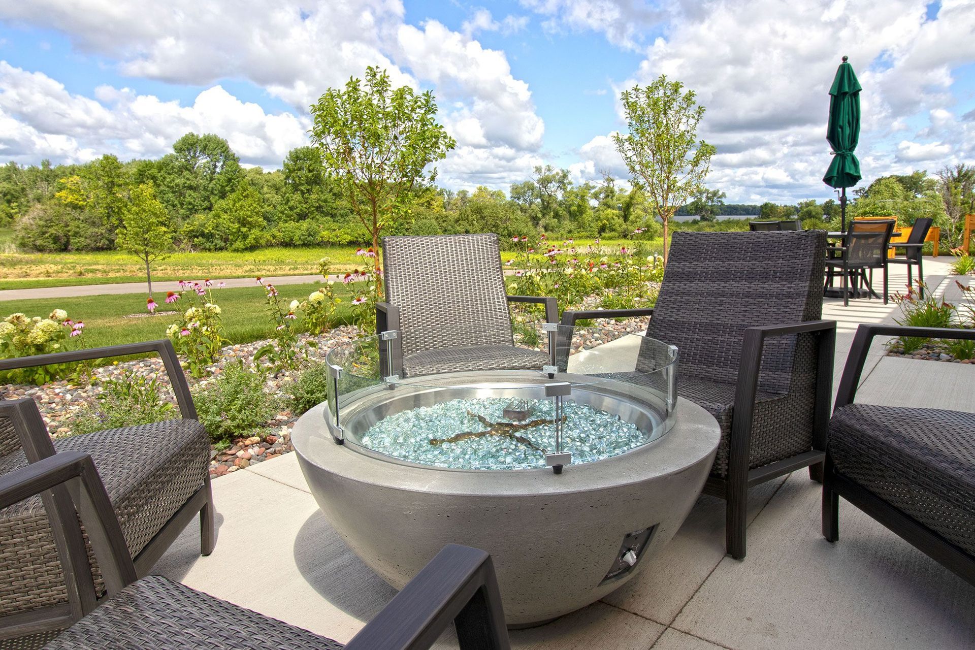 A fire pit is surrounded by chairs and umbrellas on a patio.