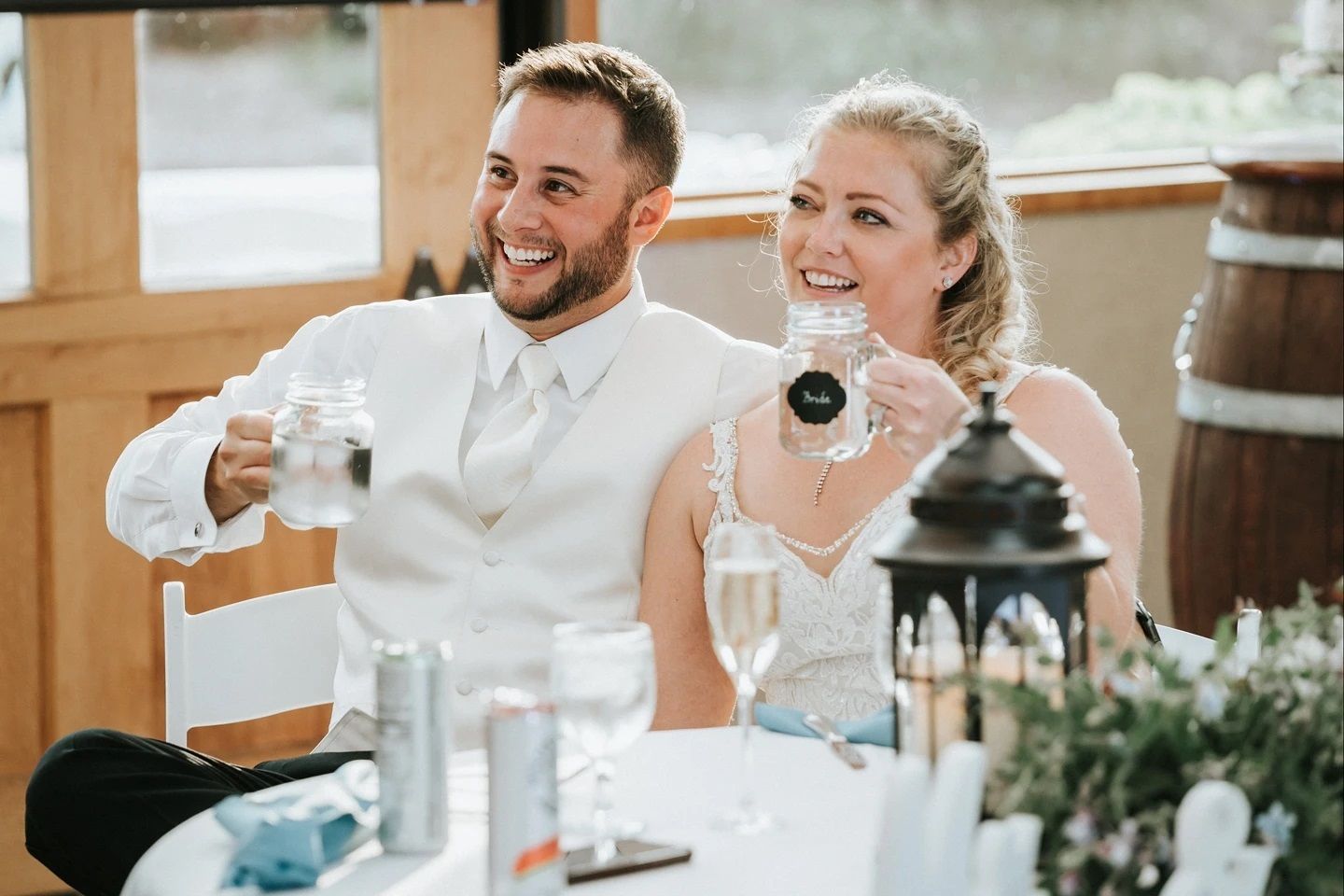 A bride and groom are sitting at a table toasting with champagne.