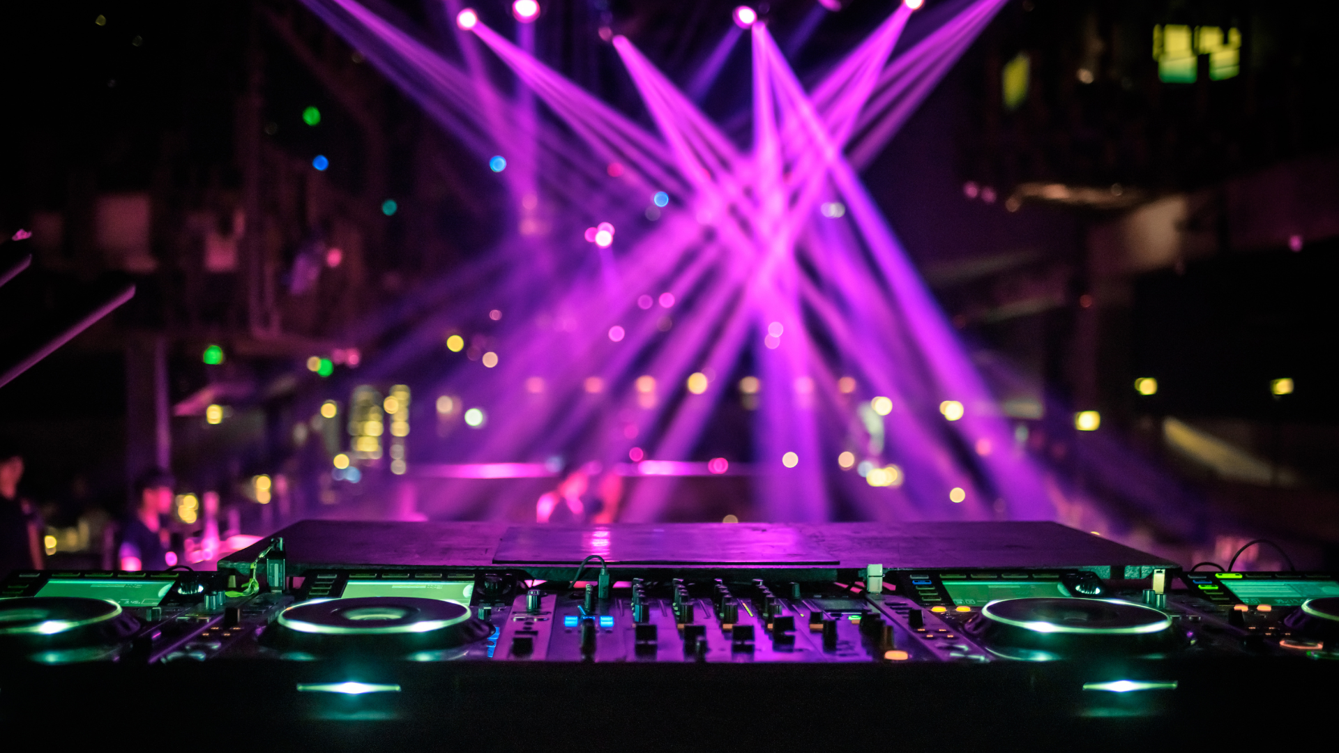 A dj is playing music in front of a stage with purple lights.