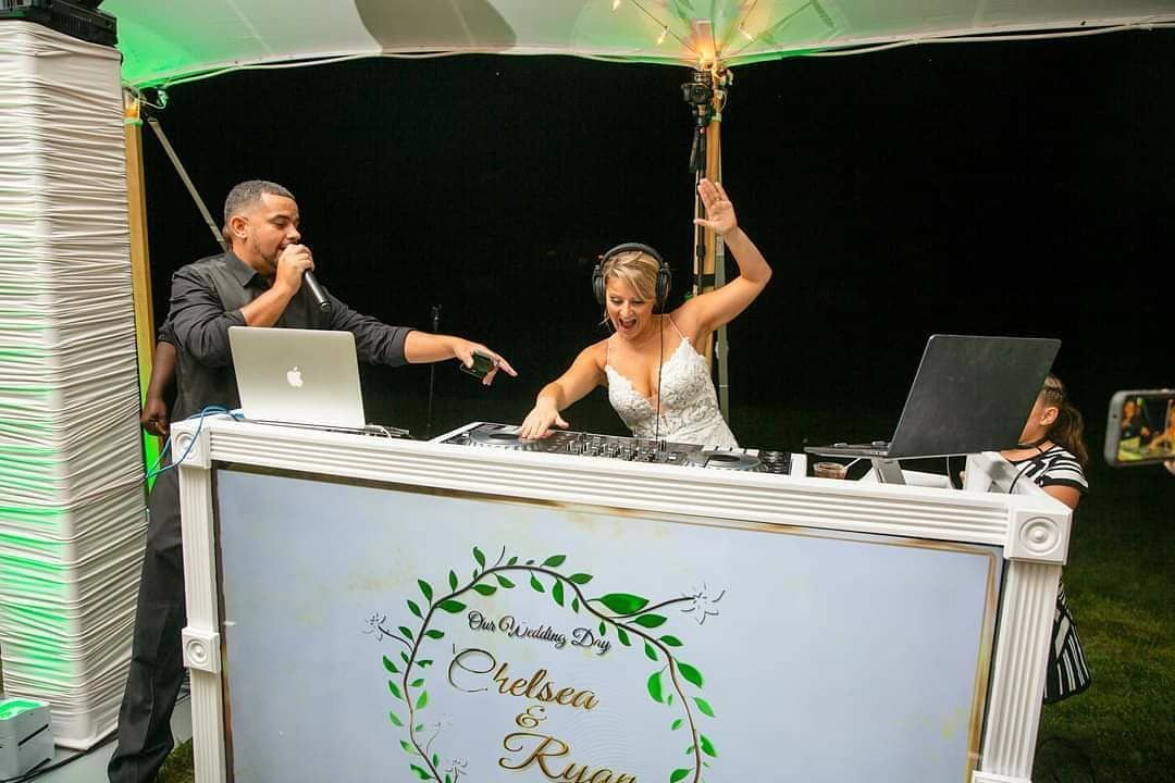 A bride and groom are dancing in front of a dj at a wedding reception.