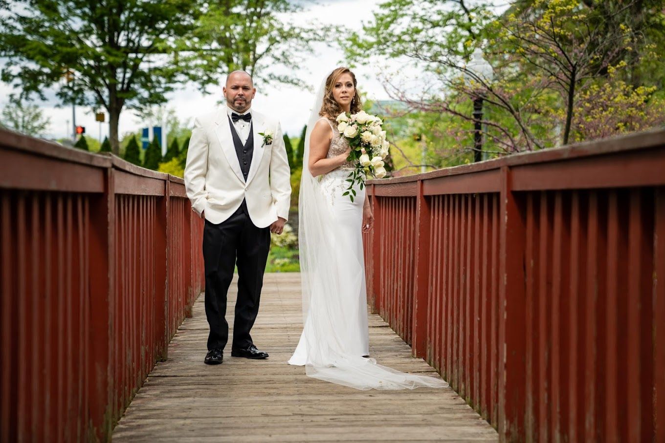 A bride and groom are walking across a wooden bridge.