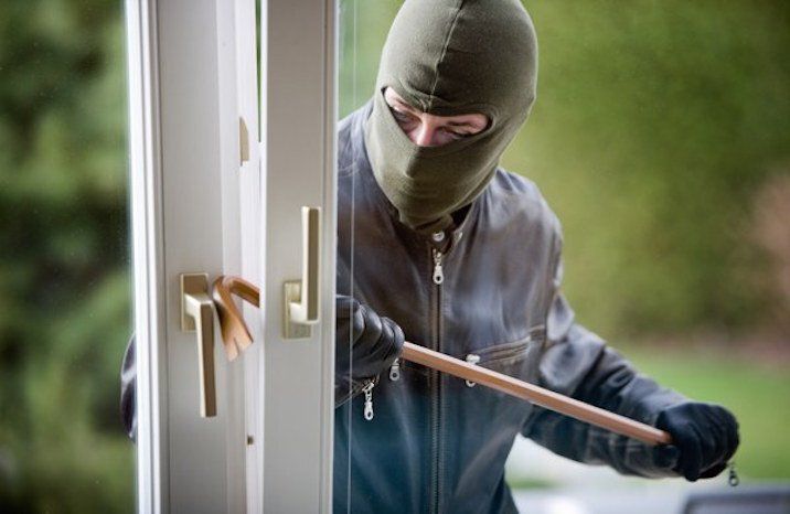A man in a mask is breaking into a house with a crowbar.
