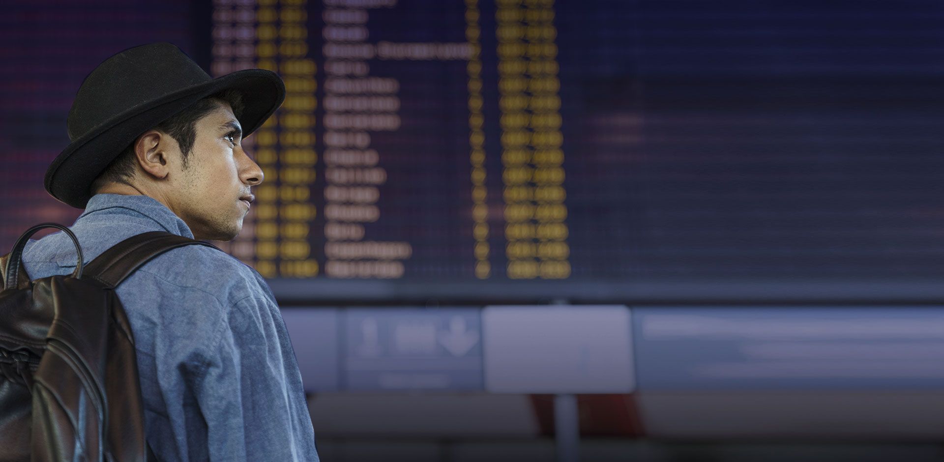 Sertanejo com chapéu de cowboy em frente ao painel de voos do aeroporto