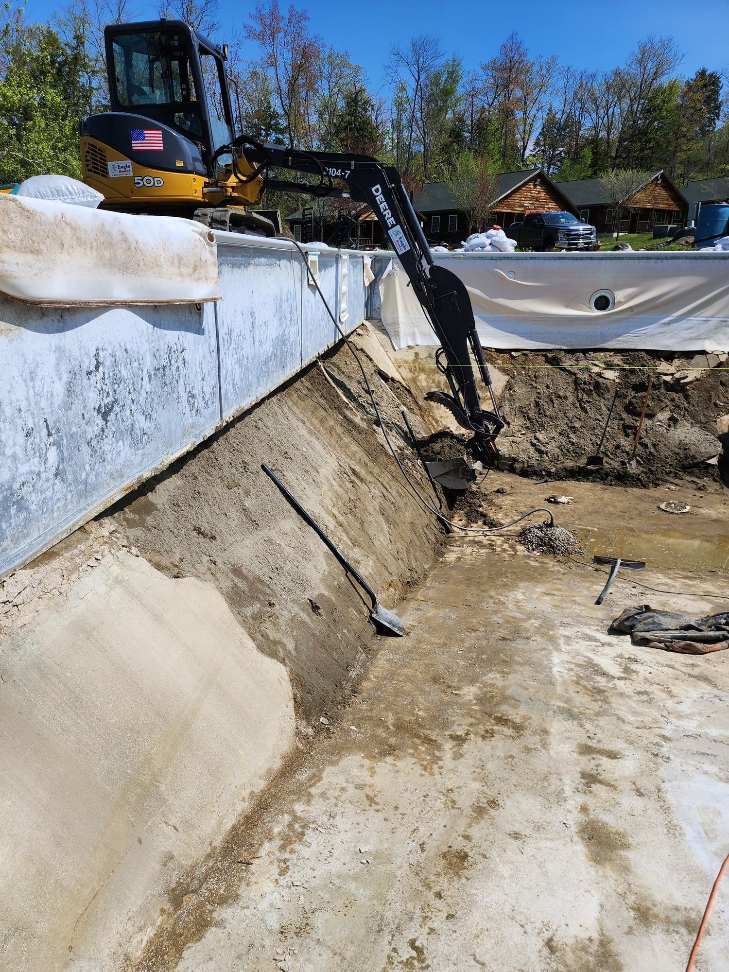 An excavator is digging a hole in the ground next to a pool.