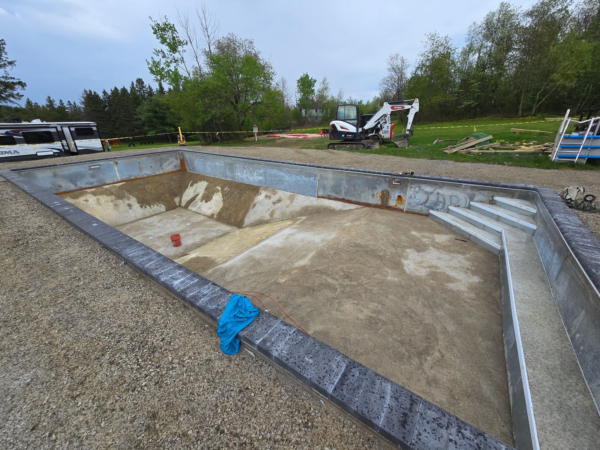 A swimming pool is being built in a yard with a bulldozer in the background.