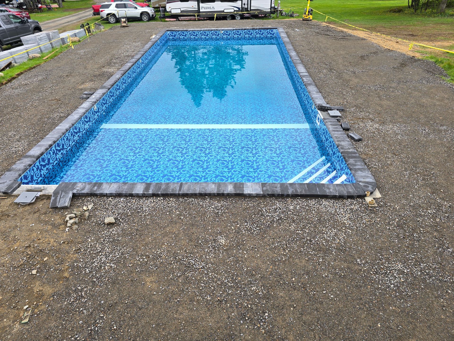 A large swimming pool is sitting in the middle of a dirt field.