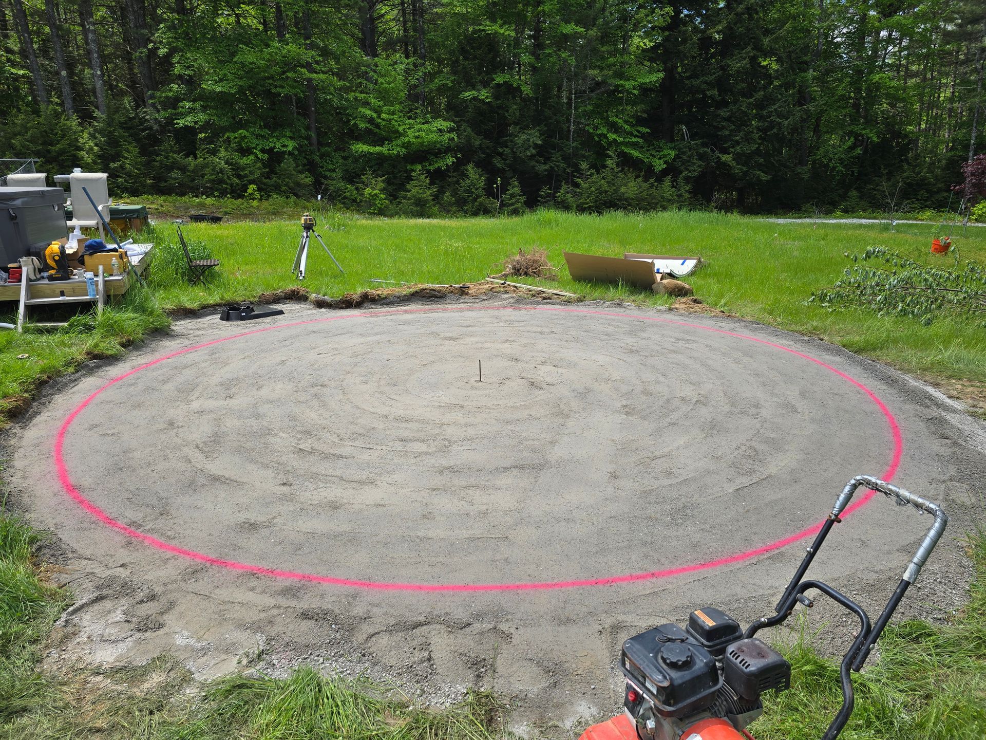 A lawn mower is sitting in the grass next to a circle of dirt.