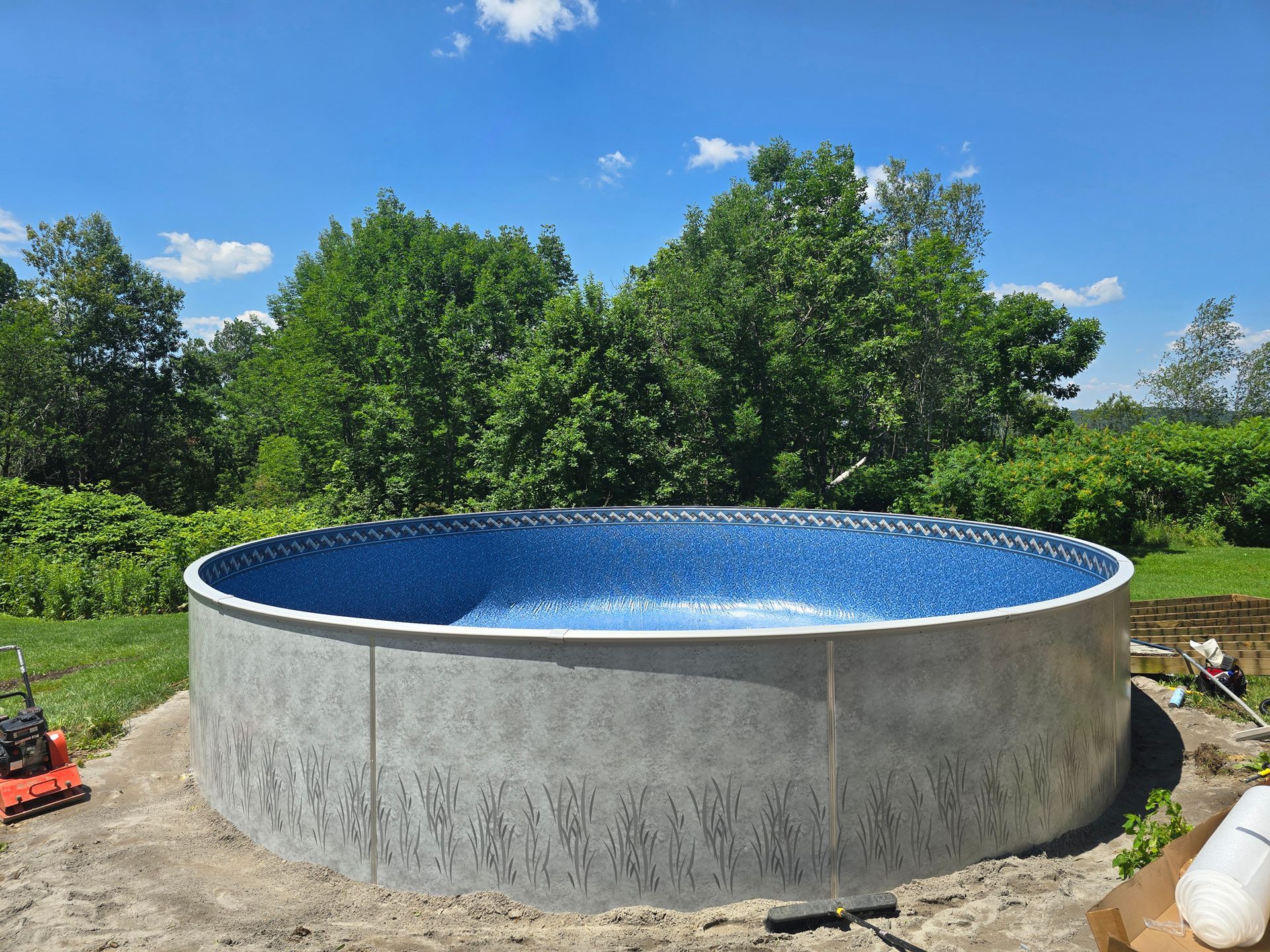A large swimming pool is being built in a backyard with trees in the background.