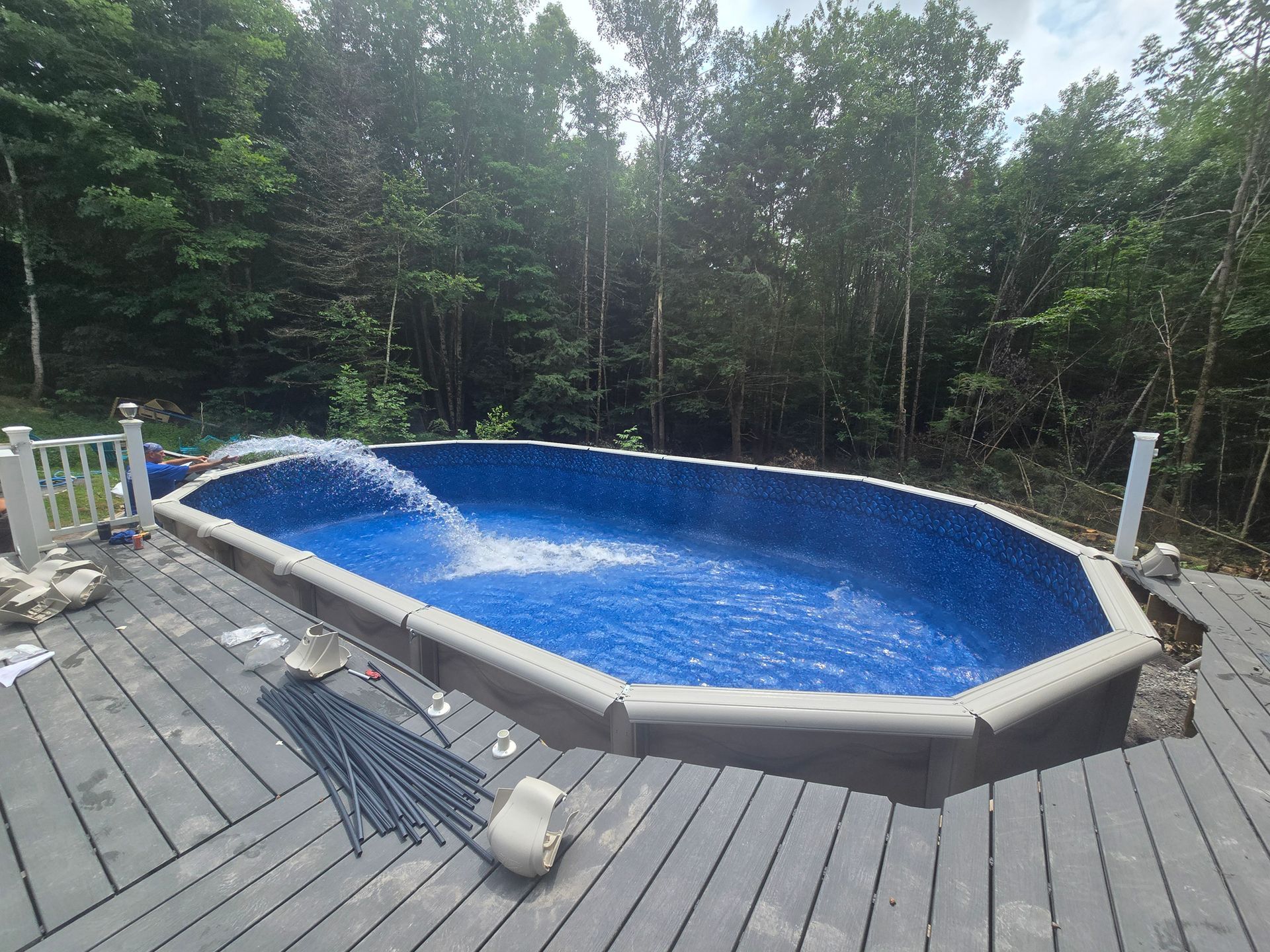 A large swimming pool is sitting on top of a wooden deck surrounded by trees.