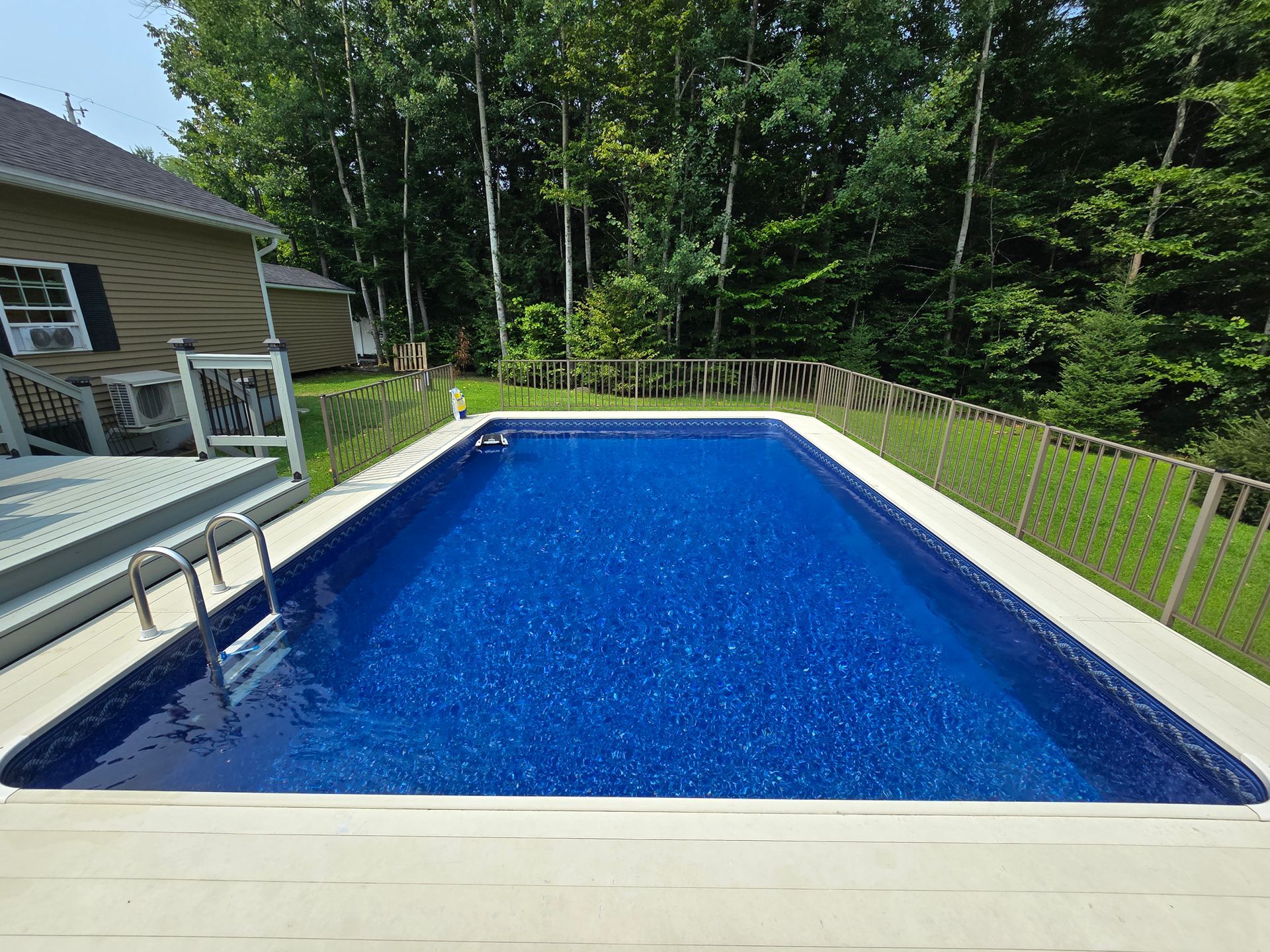 A large swimming pool in the backyard of a house surrounded by trees.
