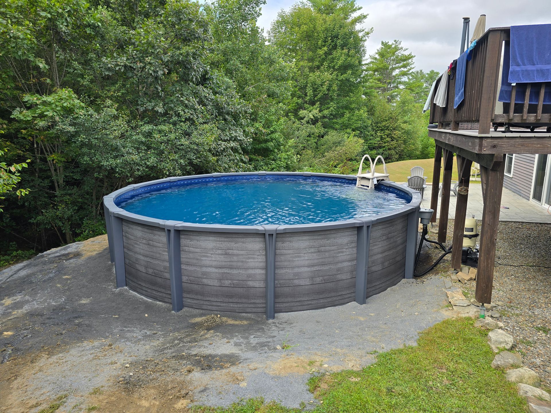 A large swimming pool is sitting on top of a dirt hill next to a house.